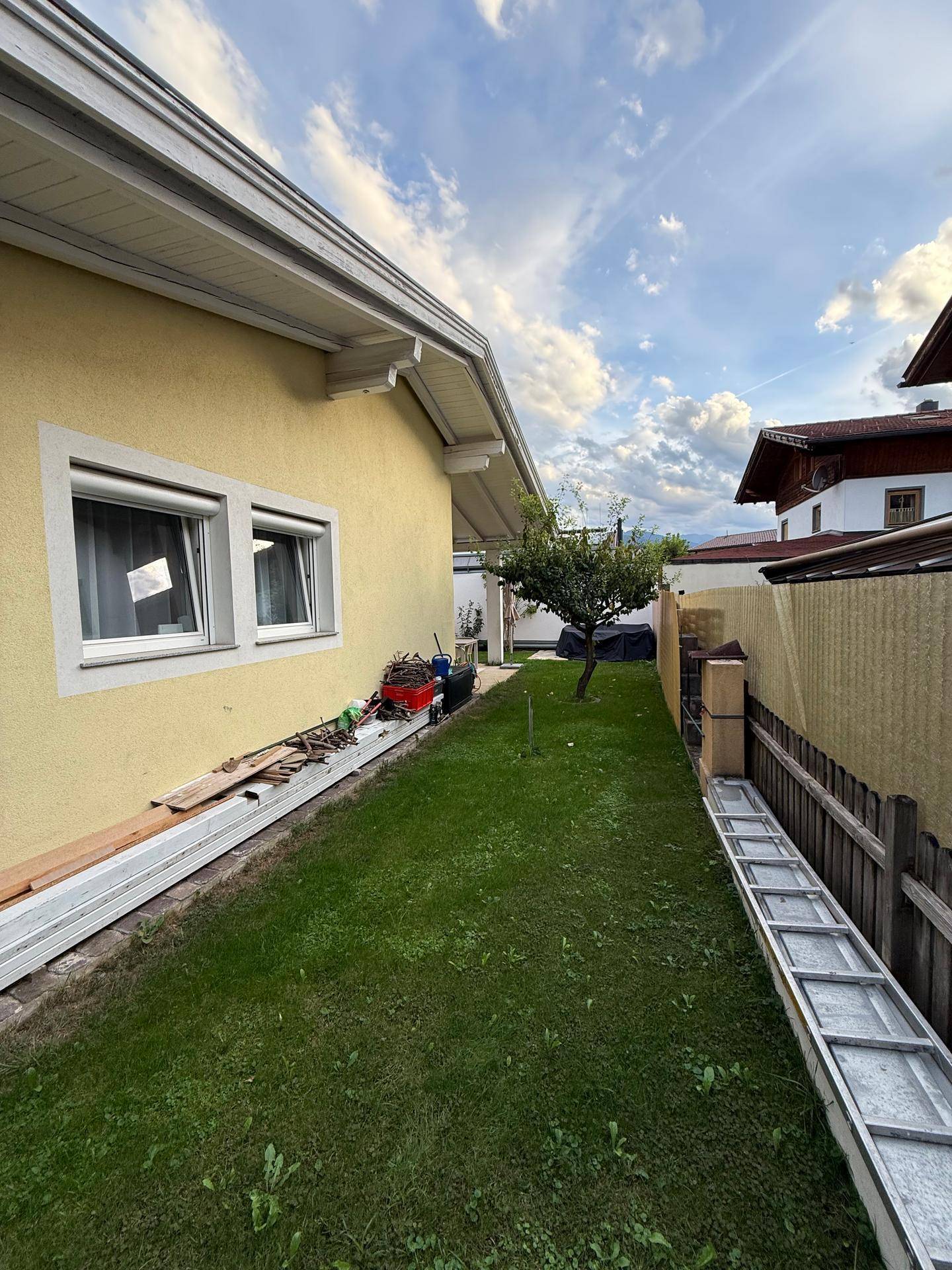 Seitlicher Gartenbereich mit Rasenfläche, kleinem Baum und Blick auf die umliegende Natur.