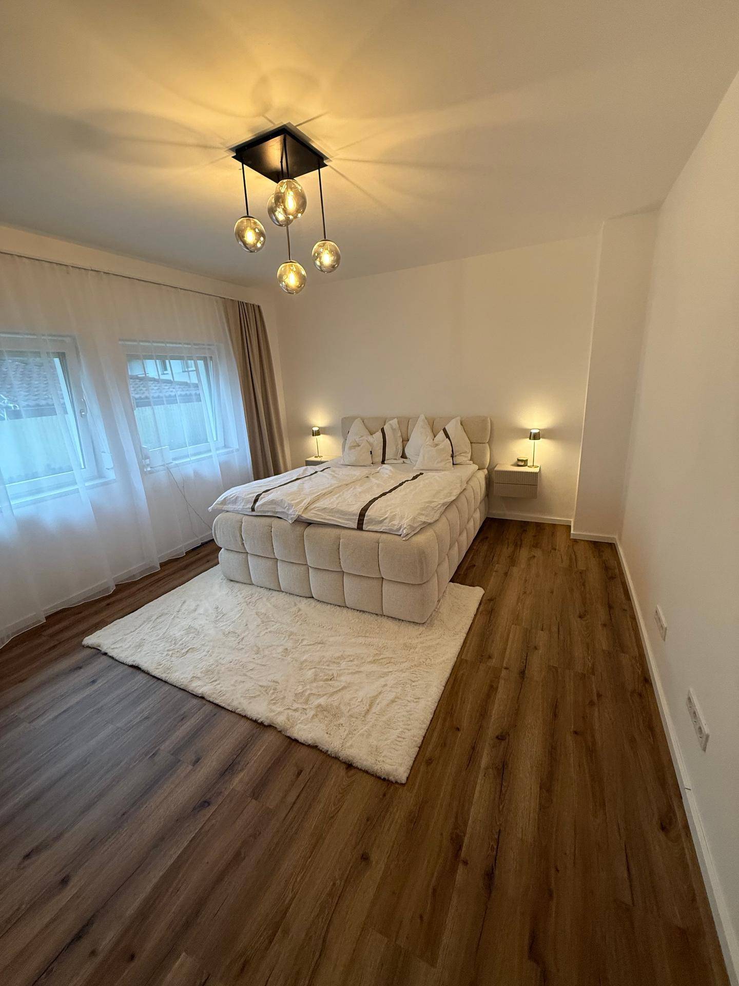 Helles Schlafzimmer mit großem Bett, modernem Deckenlicht und Holzboden.