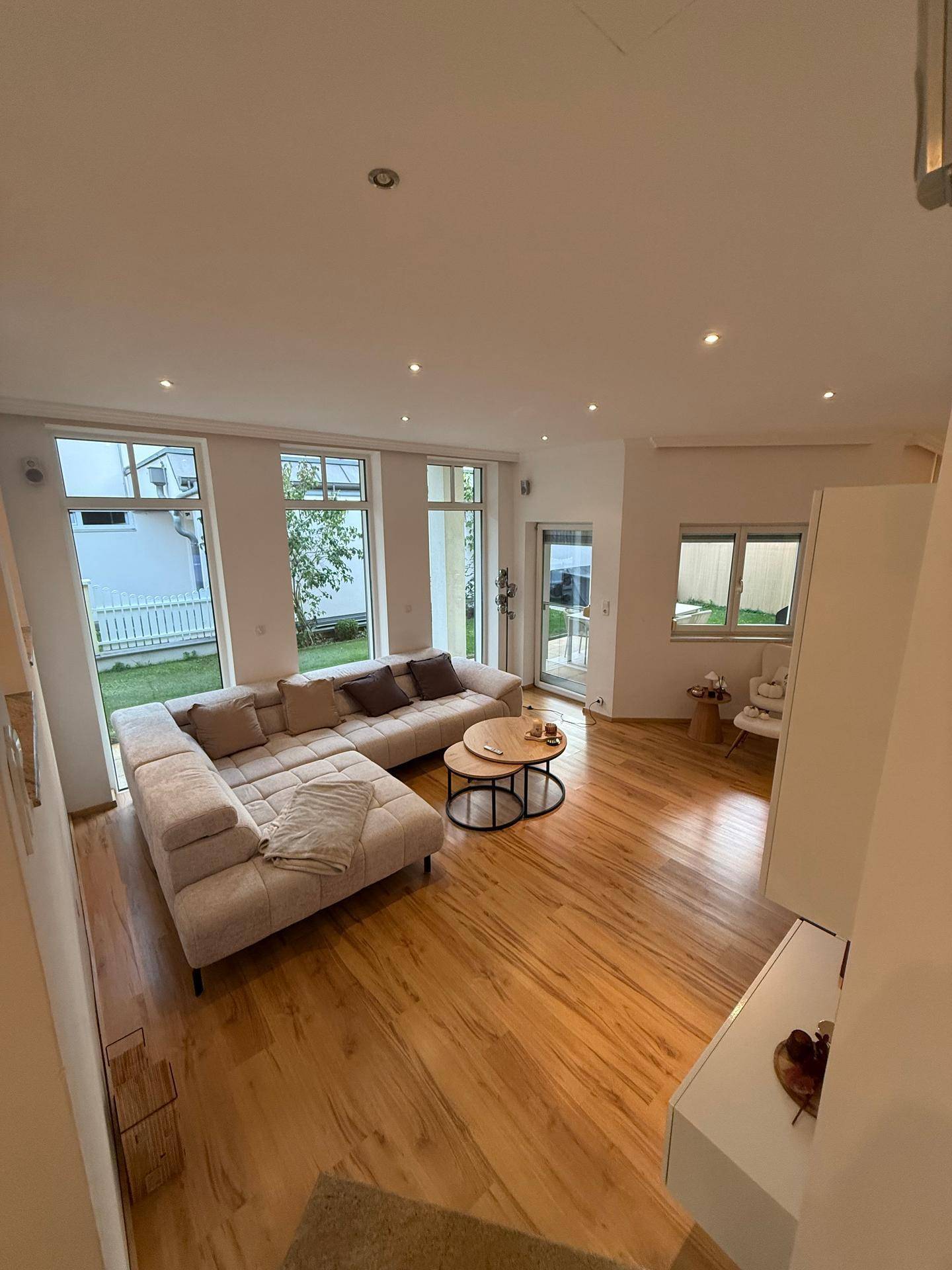 Geräumiges Wohnzimmer mit großen Fenstern, Holzboden und direktem Zugang zum Garten.