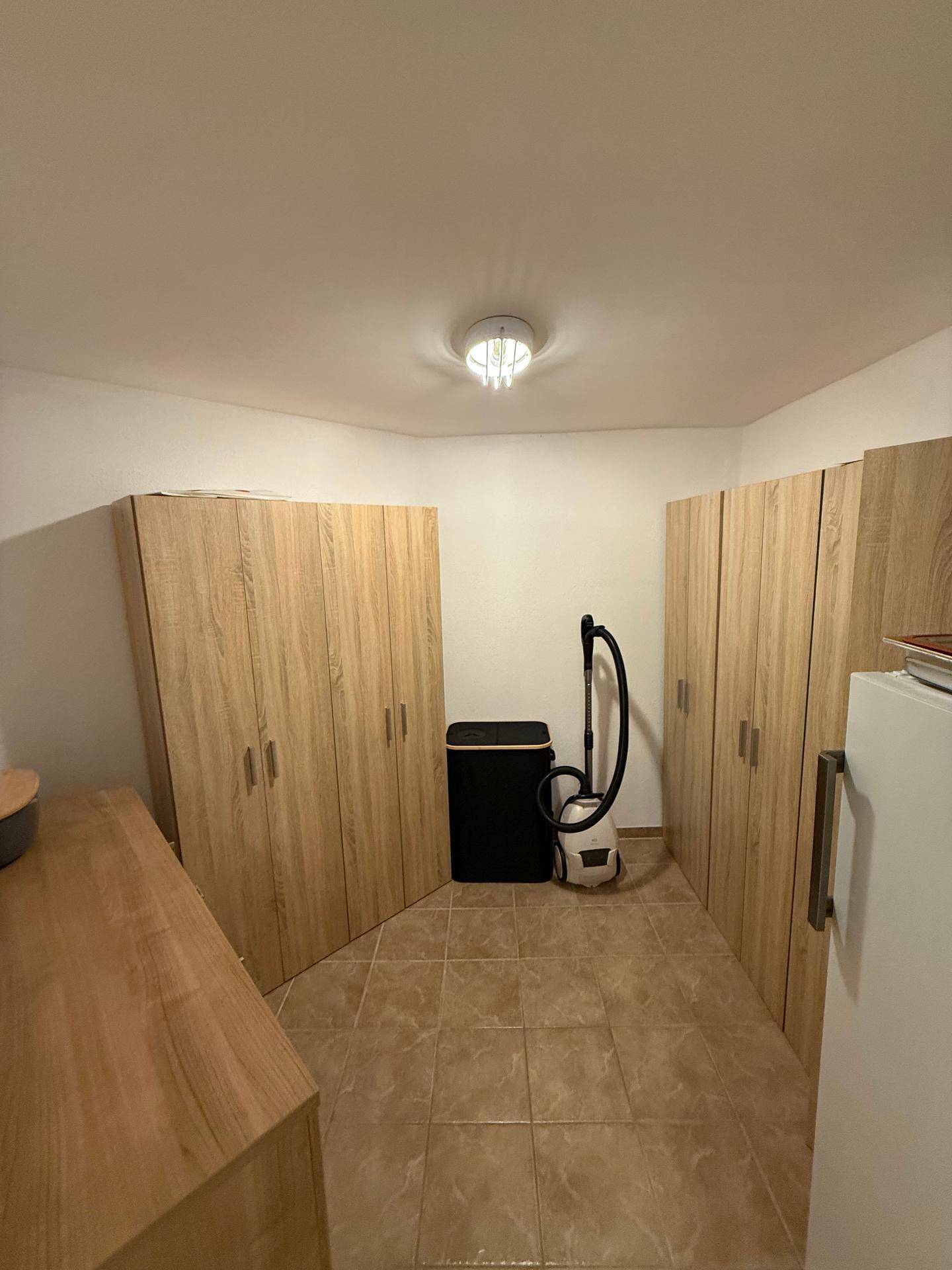 Praktischer Hauswirtschaftsraum mit Holzschränken und Fliesenboden für Stauraum.