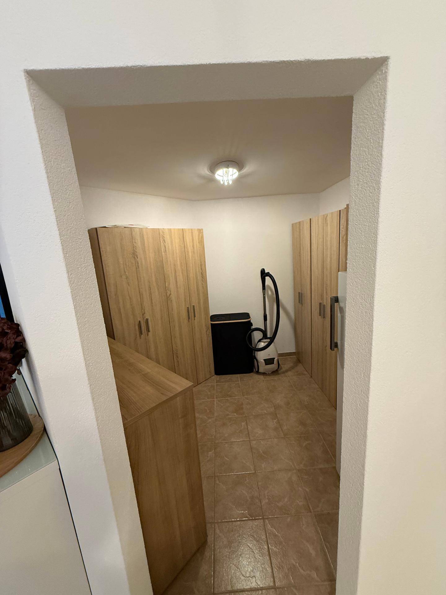 Geräumiger Abstellraum mit Holzschränken und Fliesenboden, ideal für Haushaltsgeräte.