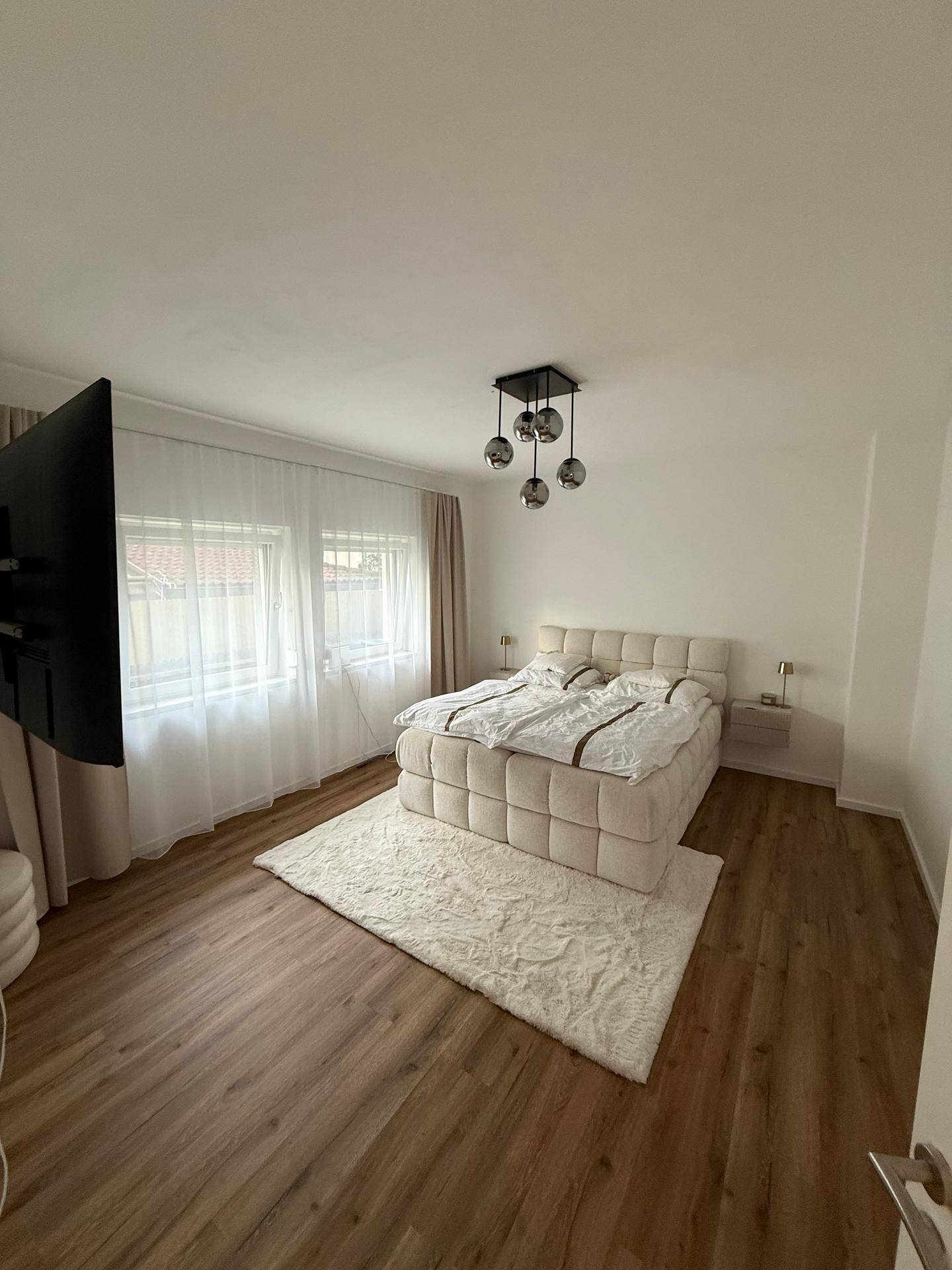Geräumiges Schlafzimmer mit Doppelbett, Wandfernseher und hellem Ambiente.