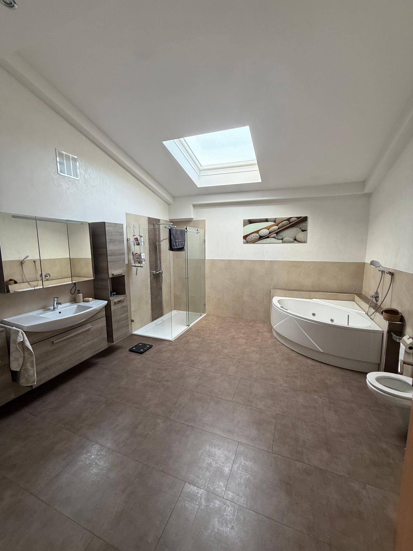 Großes Badezimmer mit Eck-Whirlpool, Duschkabine, Waschtisch und Dachfenster.