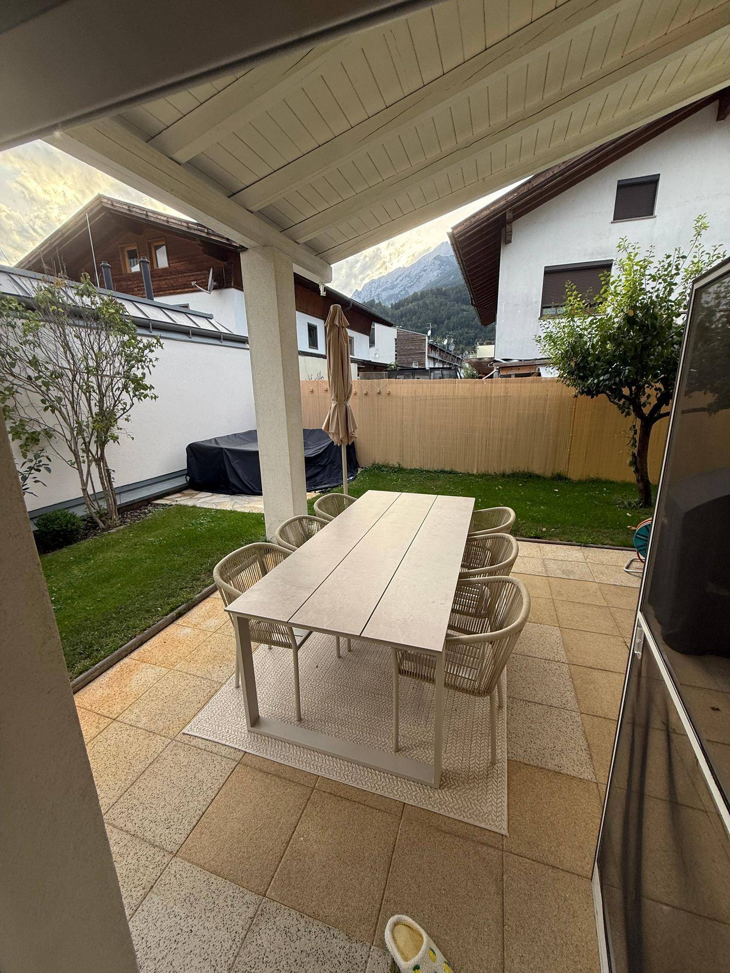 Überdachte Terrasse mit großem Esstisch und Blick auf den Garten und die Berge.