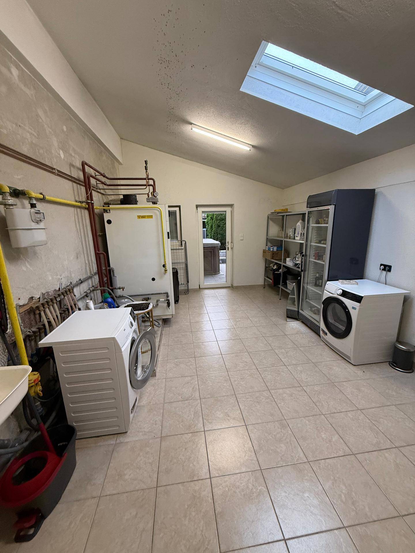 Geräumiger Hauswirtschaftsraum mit Waschmaschinen, Warmwasserbereiter und Zugang zum Außenbereich.