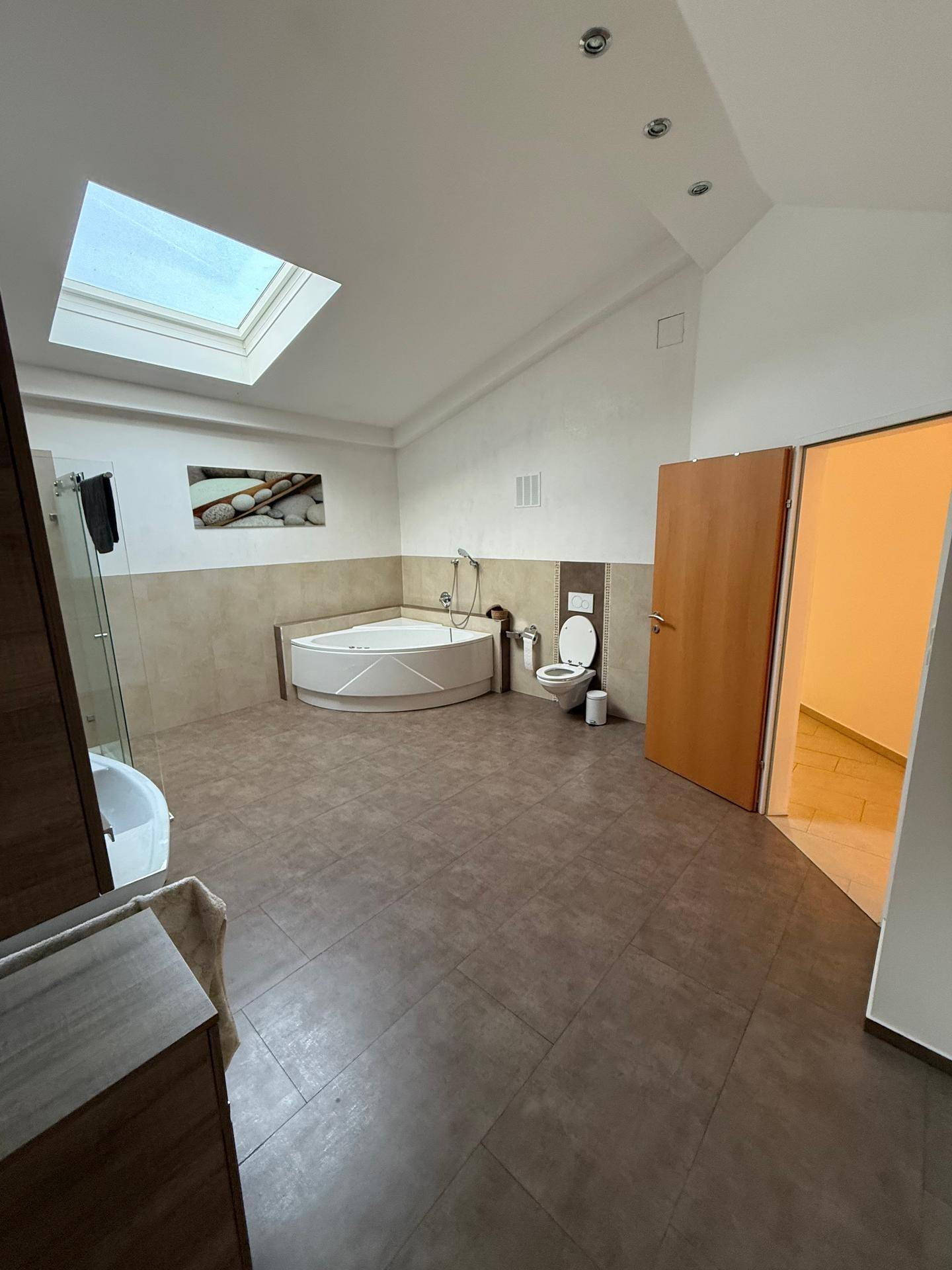 Geräumiges Badezimmer mit Eck-Whirlpool, Toilette und hellem Dachfenster.