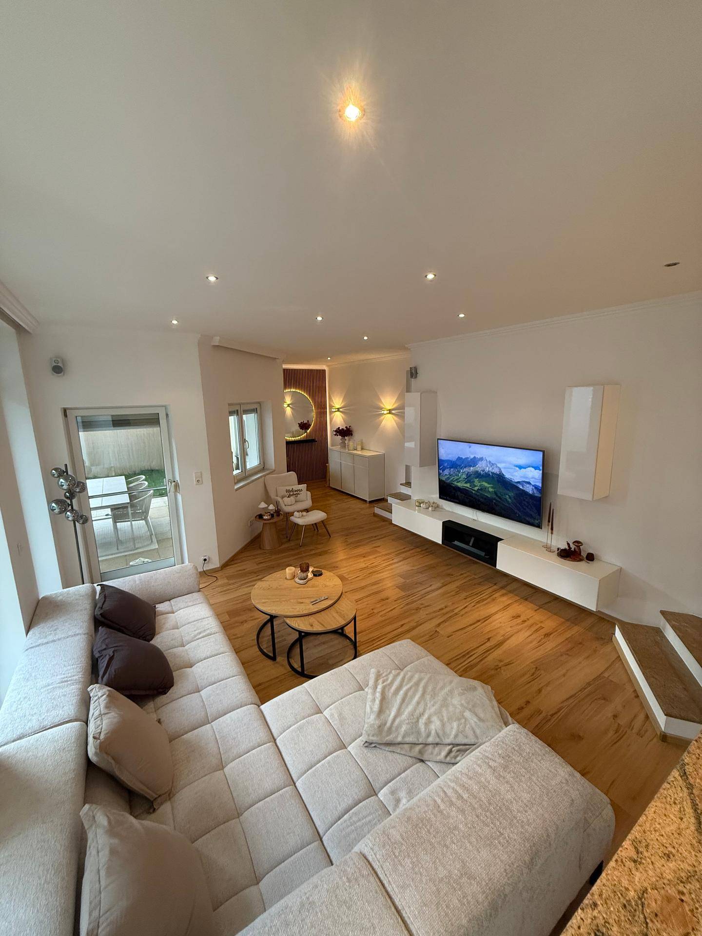 Helles Wohnzimmer mit großem Ecksofa, Holzboden und Zugang zum Gartenbereich.