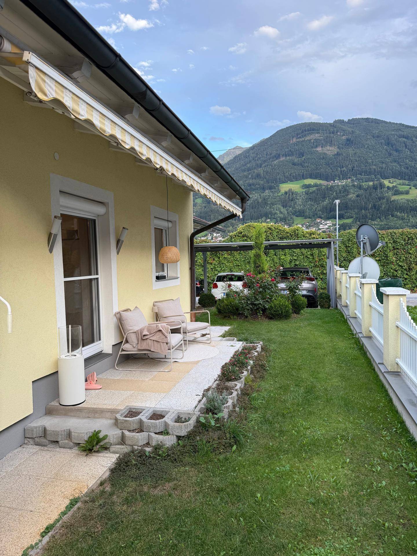 Kleiner Sitzbereich im Freien mit Rasenfläche und Blick auf die Berge und den Carport.