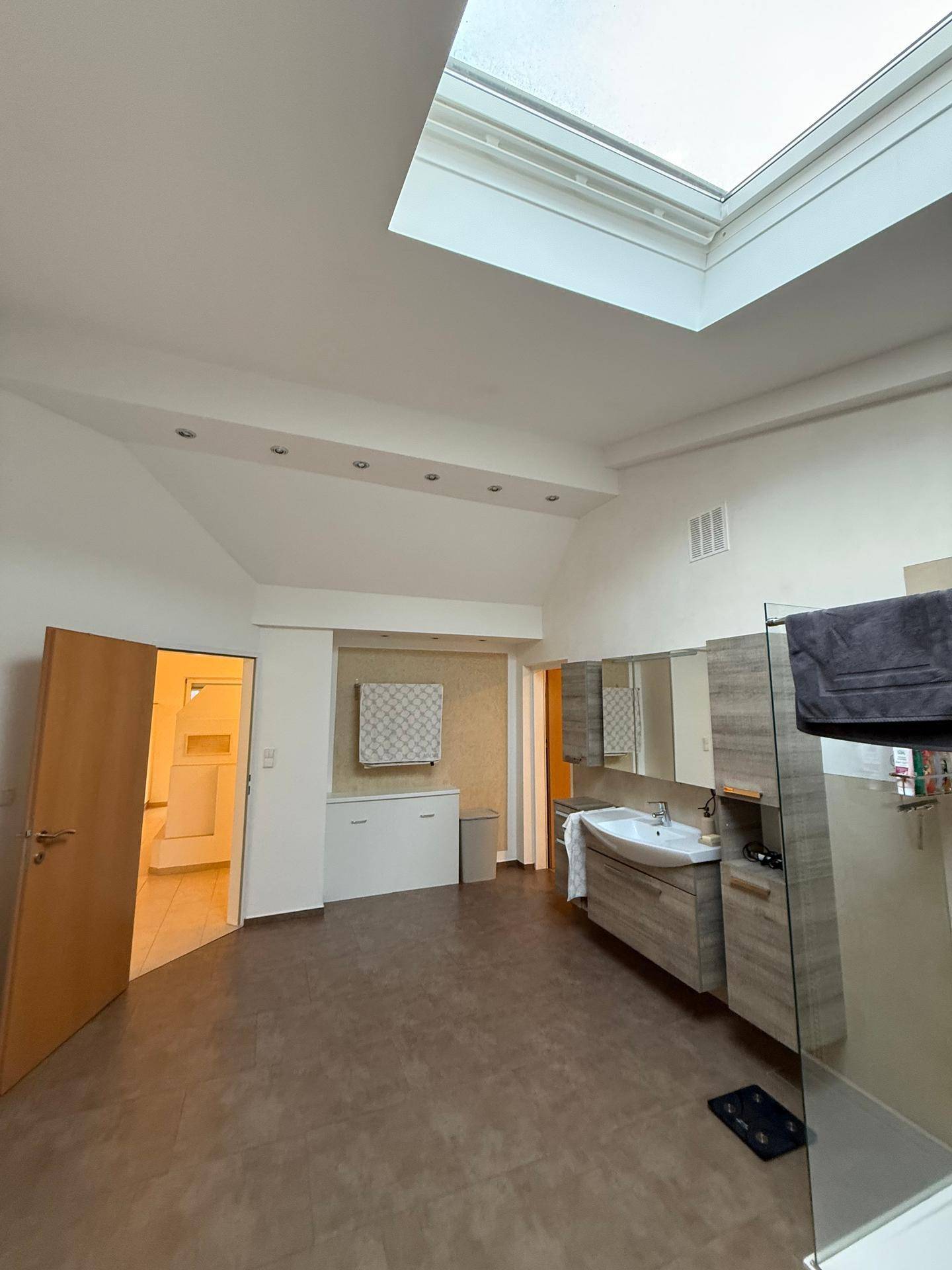 Helles Badezimmer mit Waschtisch, Duschkabine, Dachfenster und beheiztem Handtuchhalter.