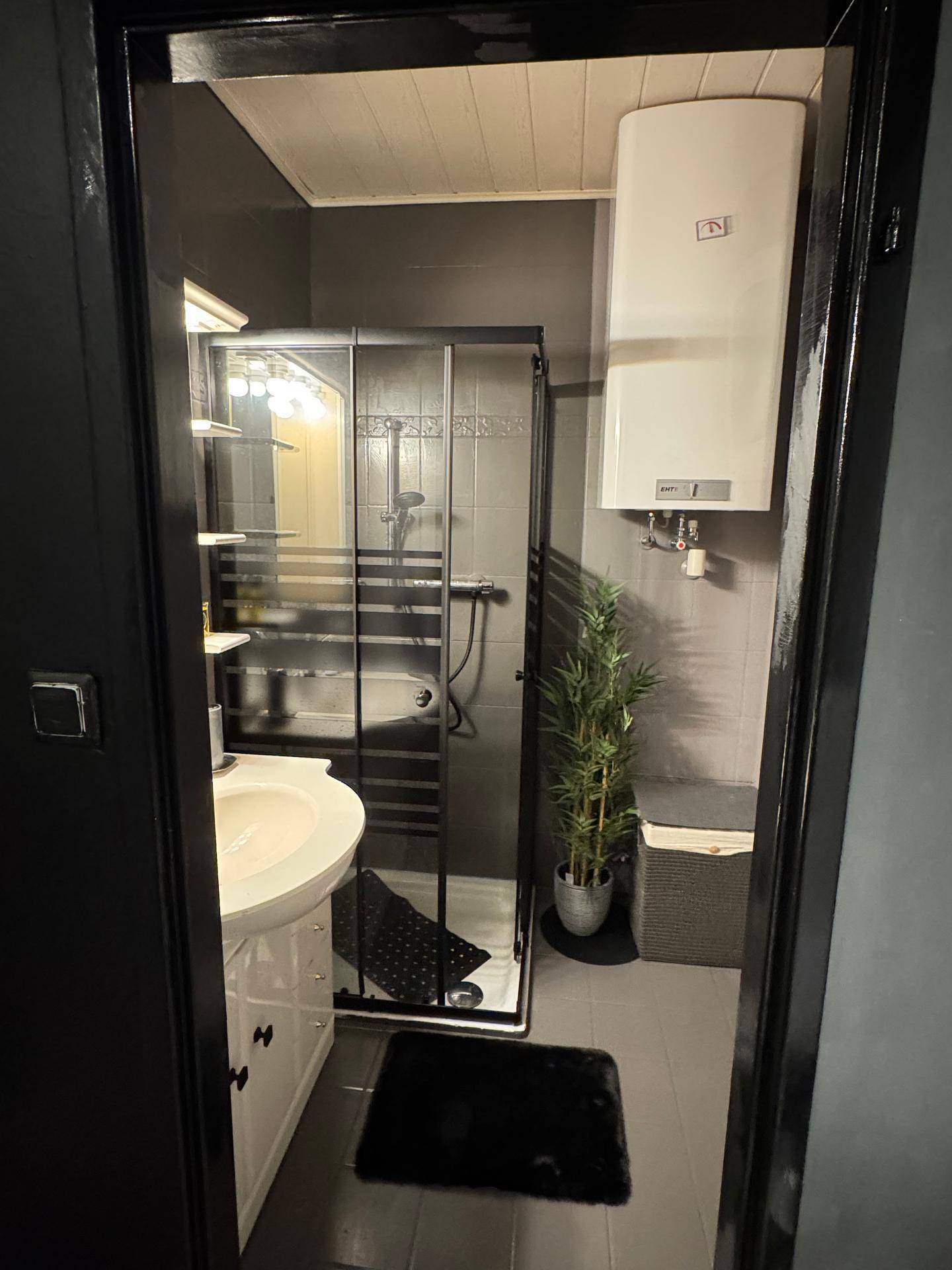 Funktionales Badezimmer mit Duschkabine, Waschbecken und einem an der Wand montierten Warmwasserboiler.