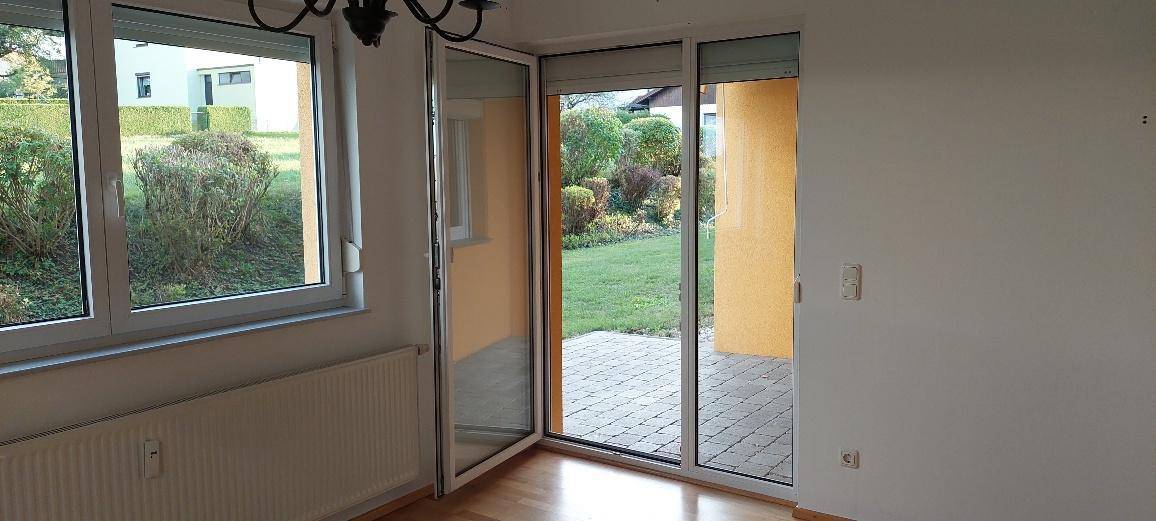 Große Glastür und Fenster bieten Zugang zu einer gepflasterten Terrasse und dem Gartenbereich.