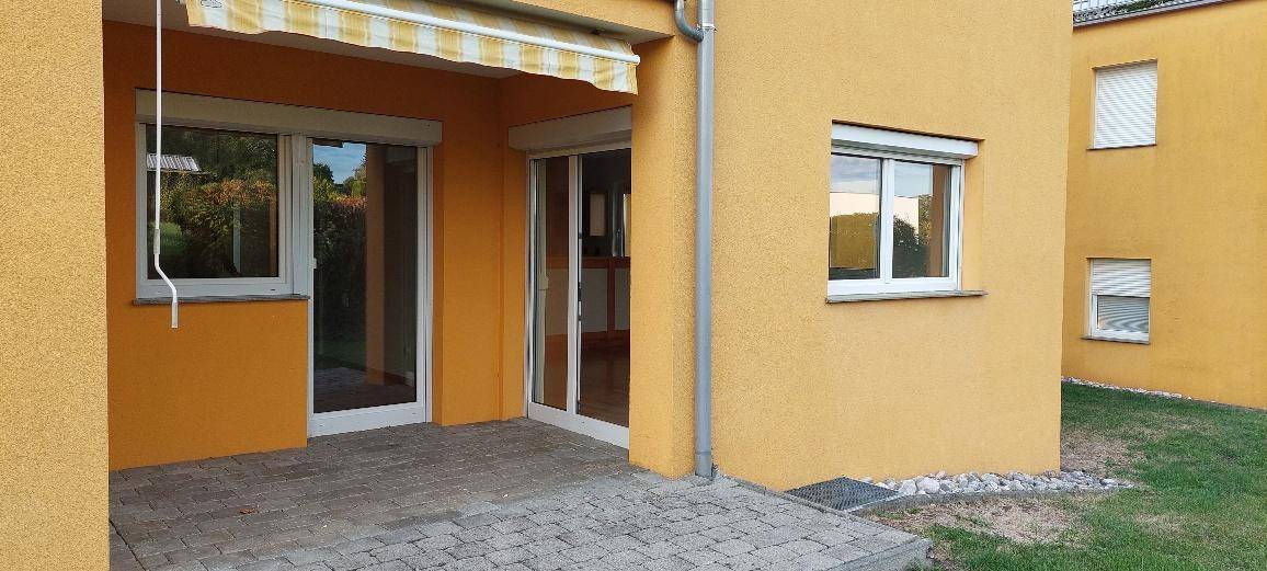 Gepflasterte Terrasse mit Markise, angrenzendem Rasen und Zugang zum Gebäude.