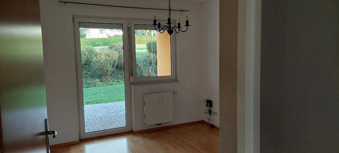 Wohnraum mit Holzboden, Heizkörper und Zugang zur Terrasse oder zum Garten durch eine Glastür.