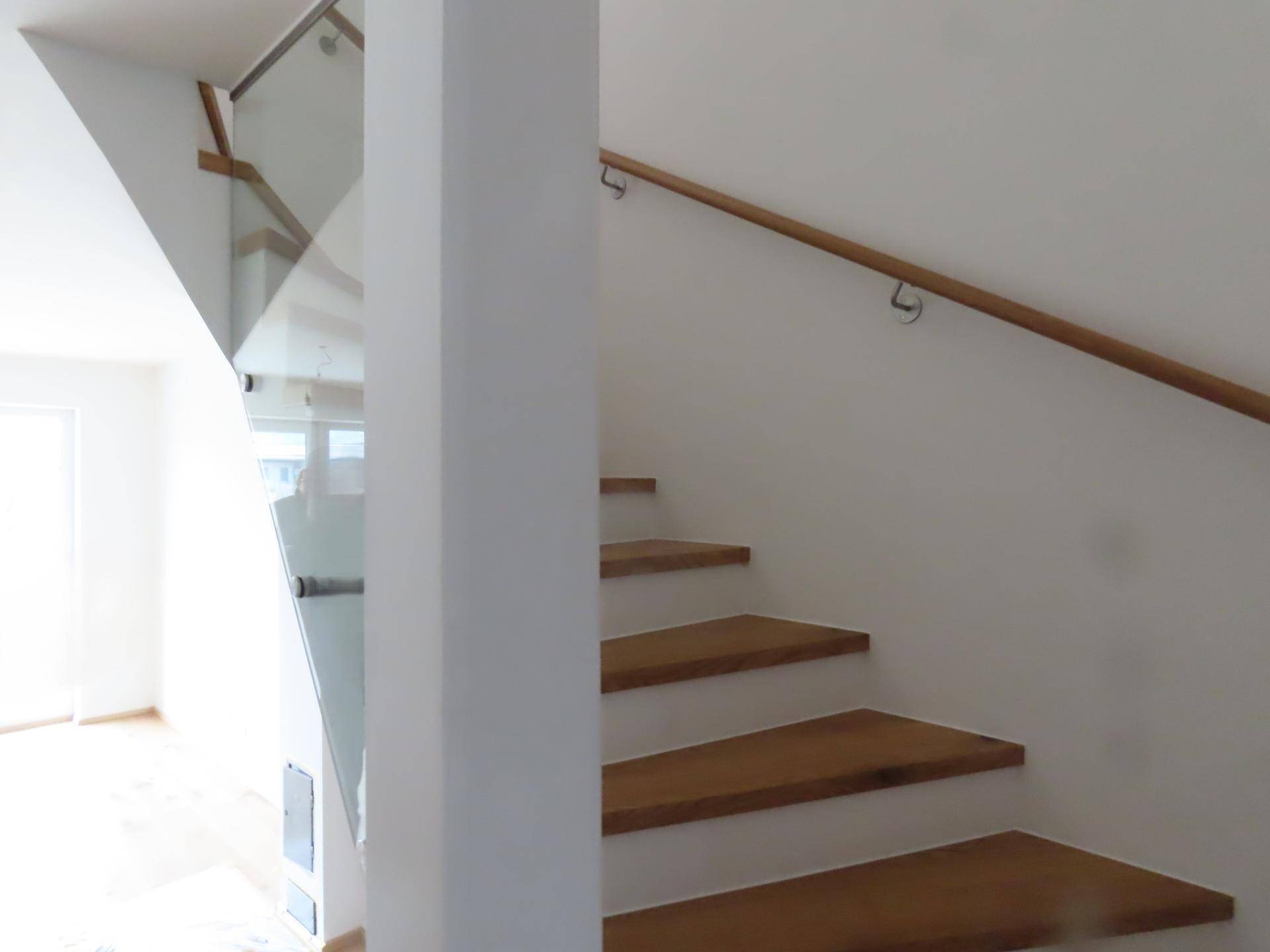 Moderne Treppe mit Holzstufen und Glasgeländer, die das Obergeschoss verbindet.