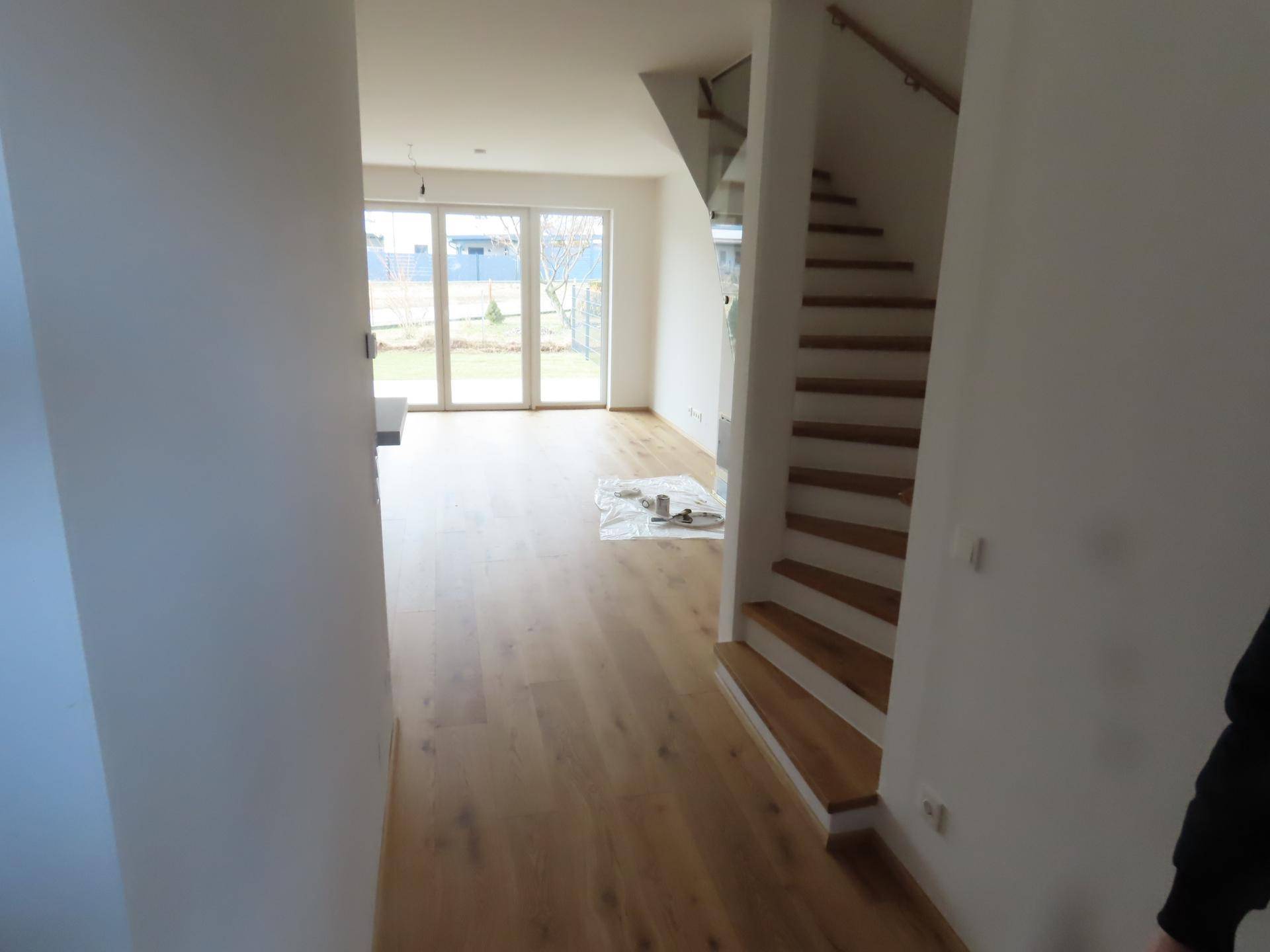 Heller Wohnbereich mit Holzboden und offener Treppe zum Obergeschoss.