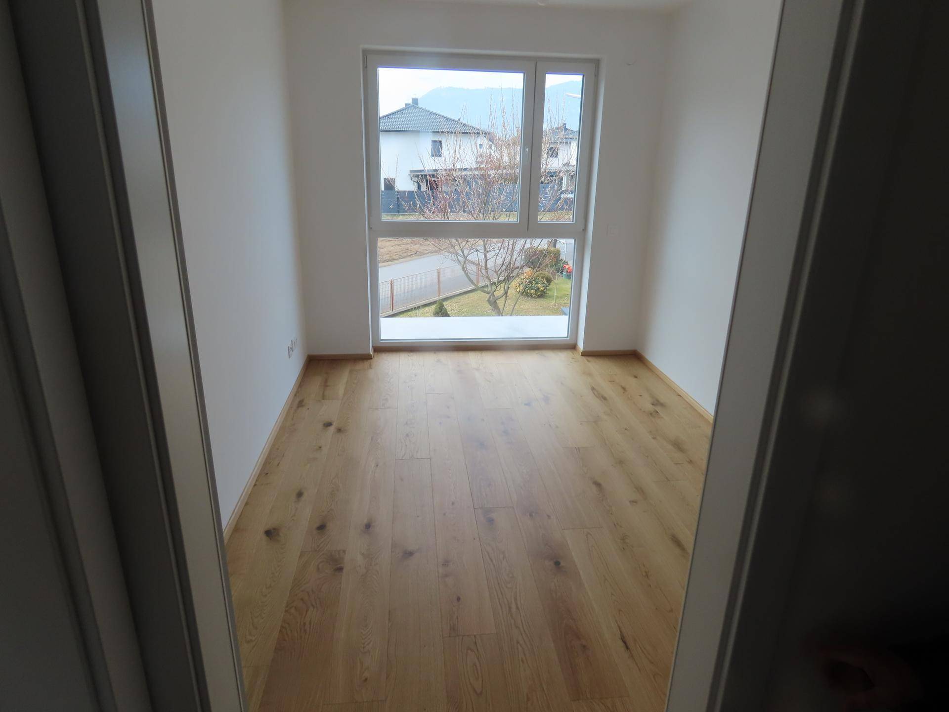 Helles Zimmer mit großem Fenster und Holzboden, ideal als Schlaf- oder Arbeitszimmer.