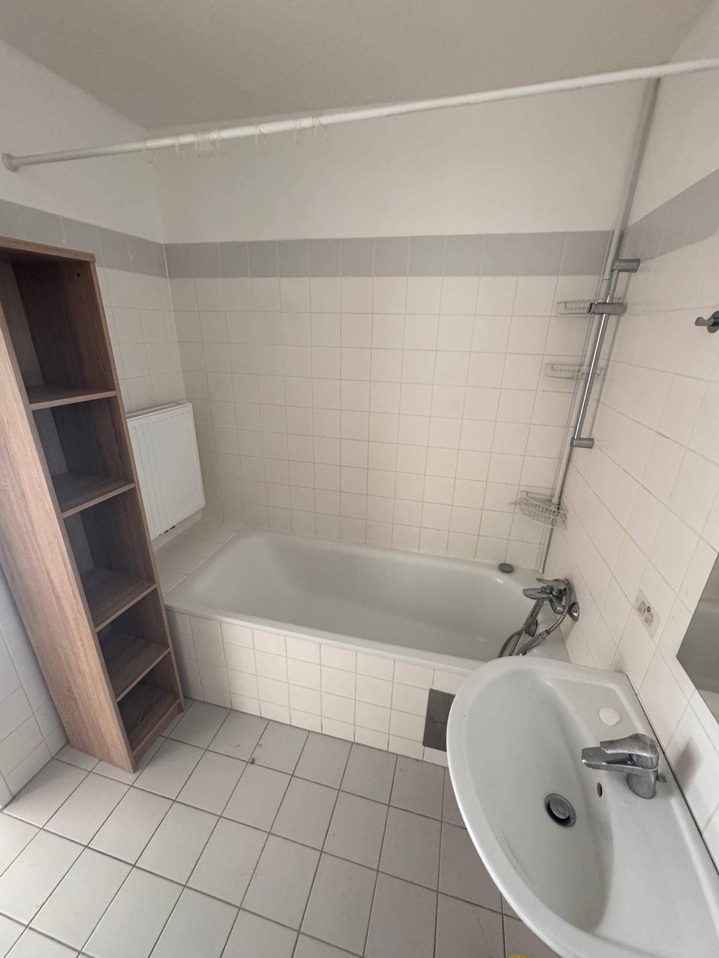 Badezimmer mit Badewanne, Waschbecken und hellen Fliesen in einem gepflegten Zustand.