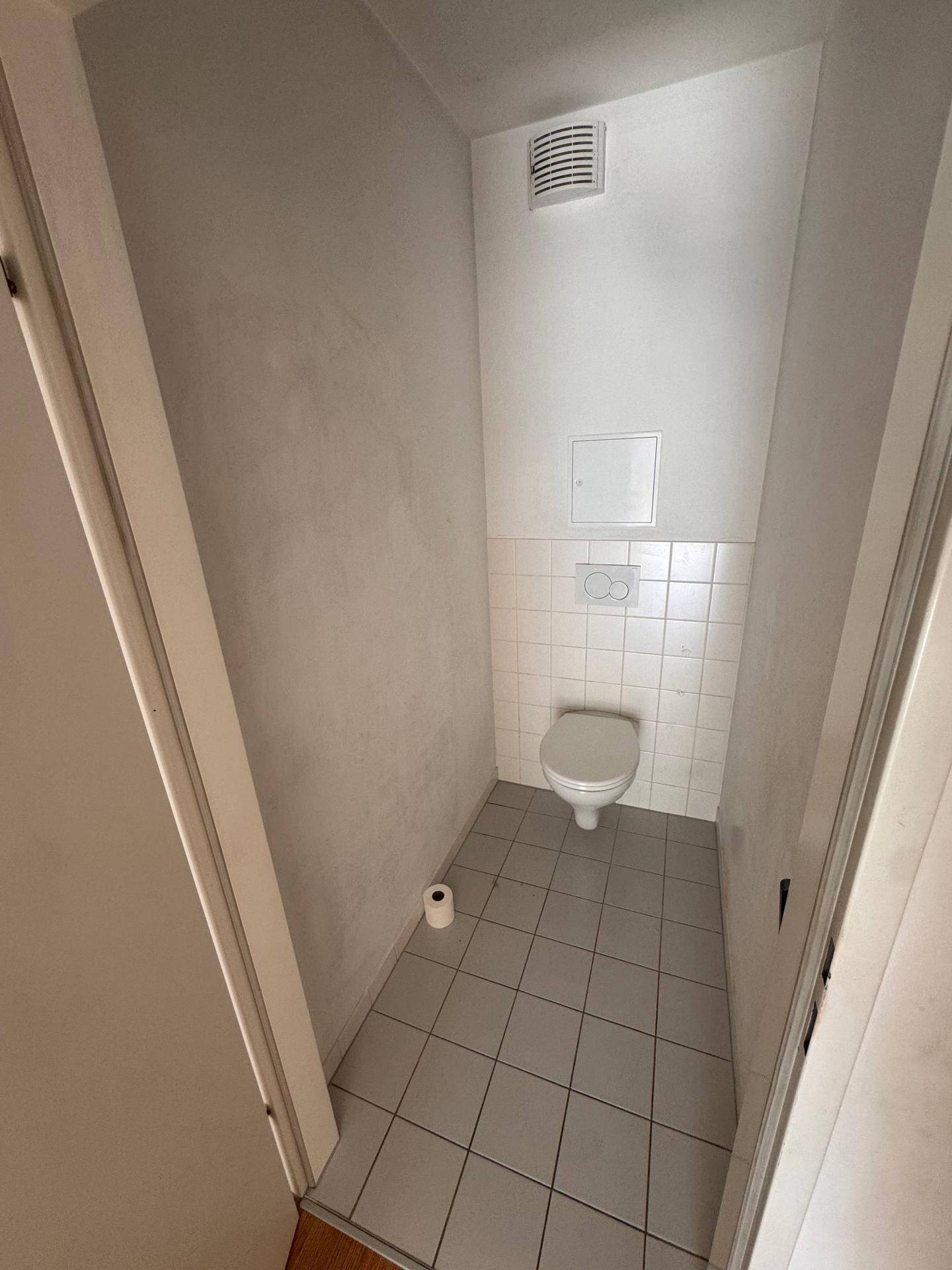 Separates WC mit Wand-WC, Fliesenboden und einem Abluftventilator für gute Belüftung.