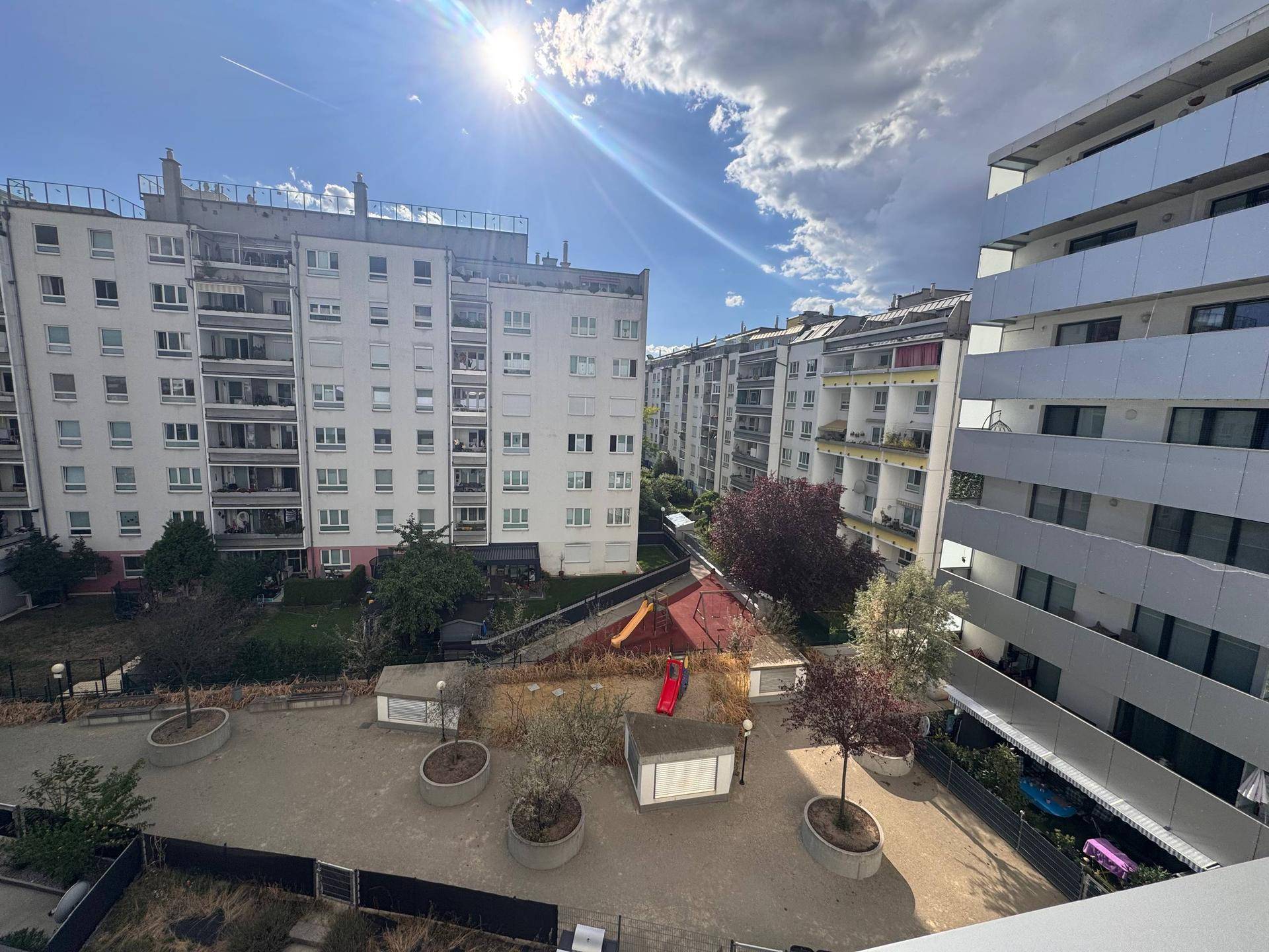 Blick auf den sonnigen Innenhof mit Spielplatz und modernen umliegenden Wohngebäuden.