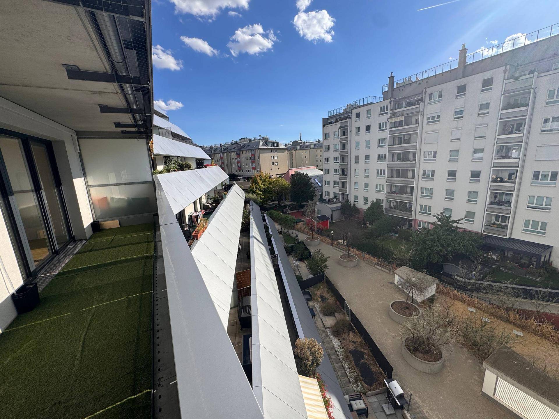 Balkon mit Kunstrasen und weitem Blick auf den begrünten Innenhof und die moderne Architektur.