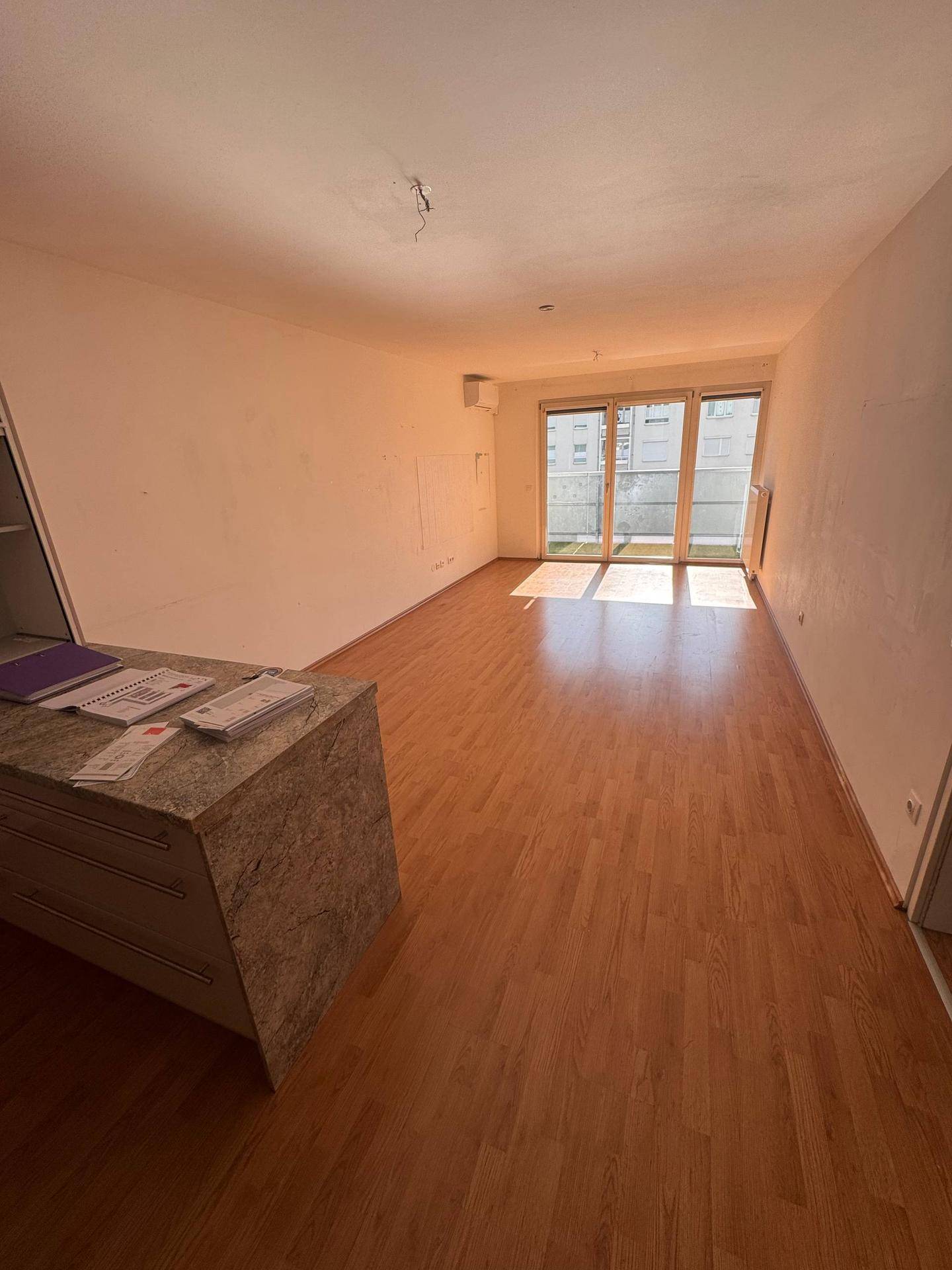 Geräumiges Wohnzimmer mit Laminatboden und großen Fenstern, die viel Tageslicht hereinlassen.