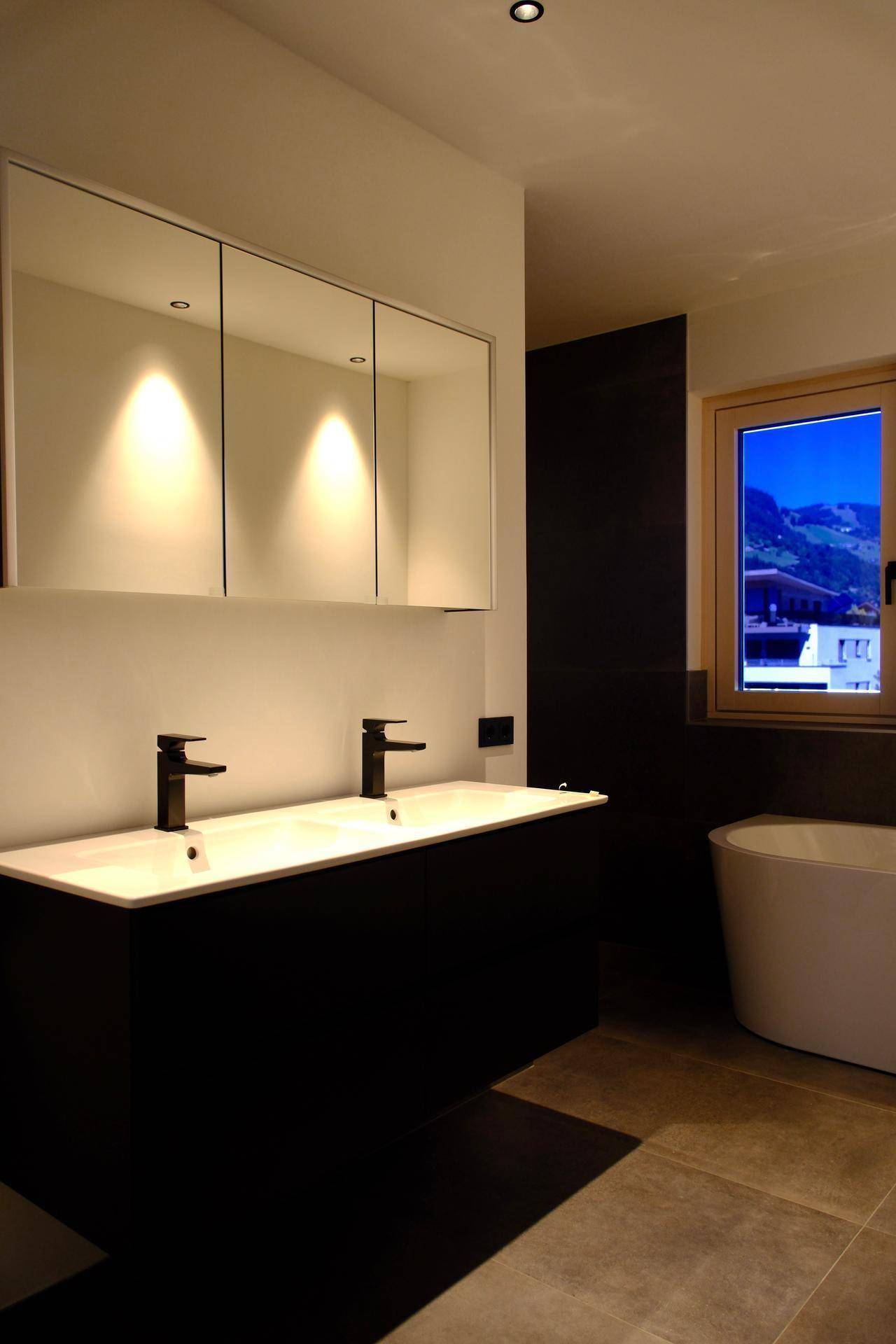 Modernes Badezimmer mit Doppelwaschbecken, dunklen Möbeln und einem Fenster mit Bergblick.