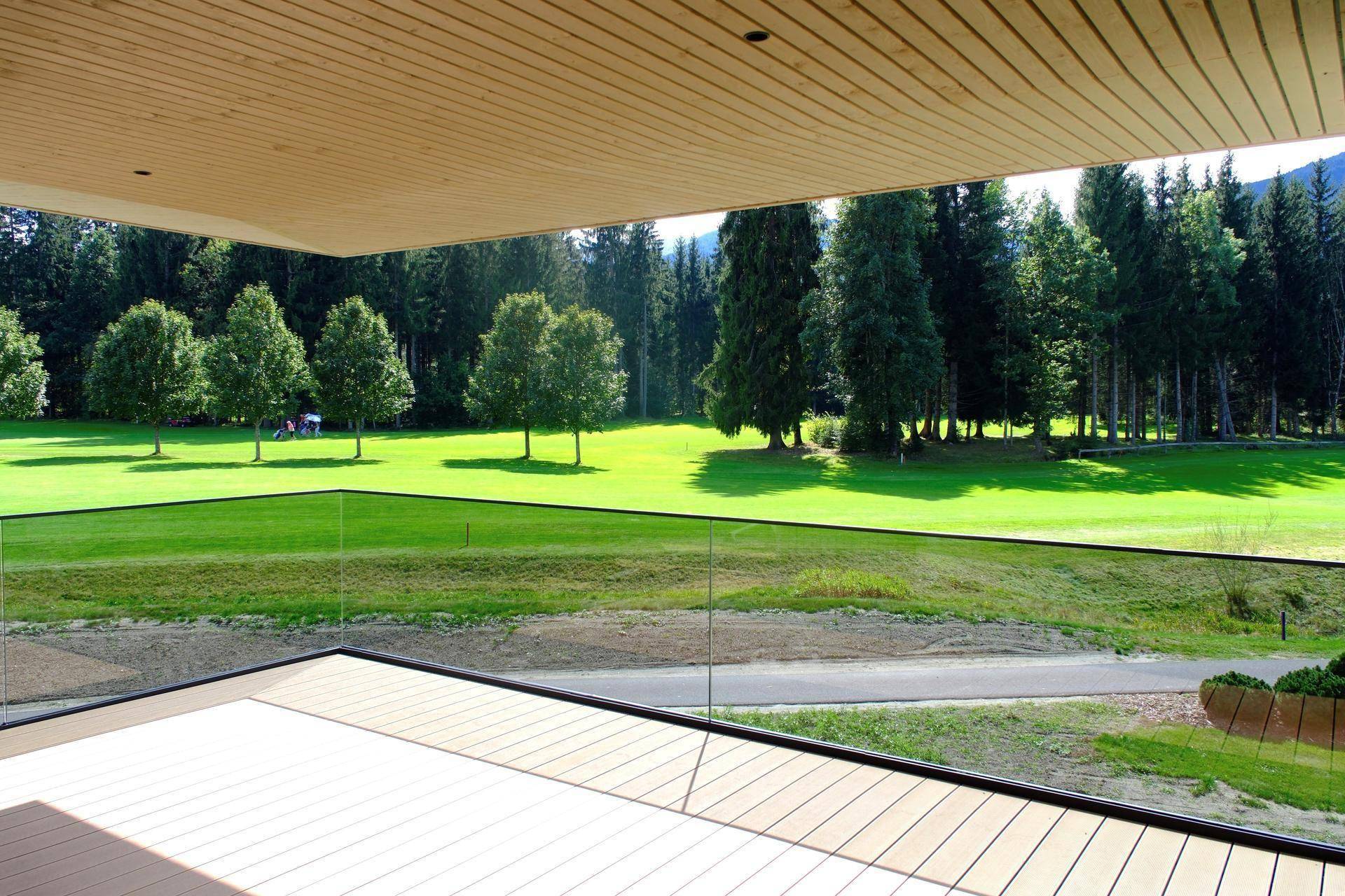 Geräumiger Balkon mit Holzboden und Glasgeländer, bietet einen weiten Blick auf den Golfplatz.