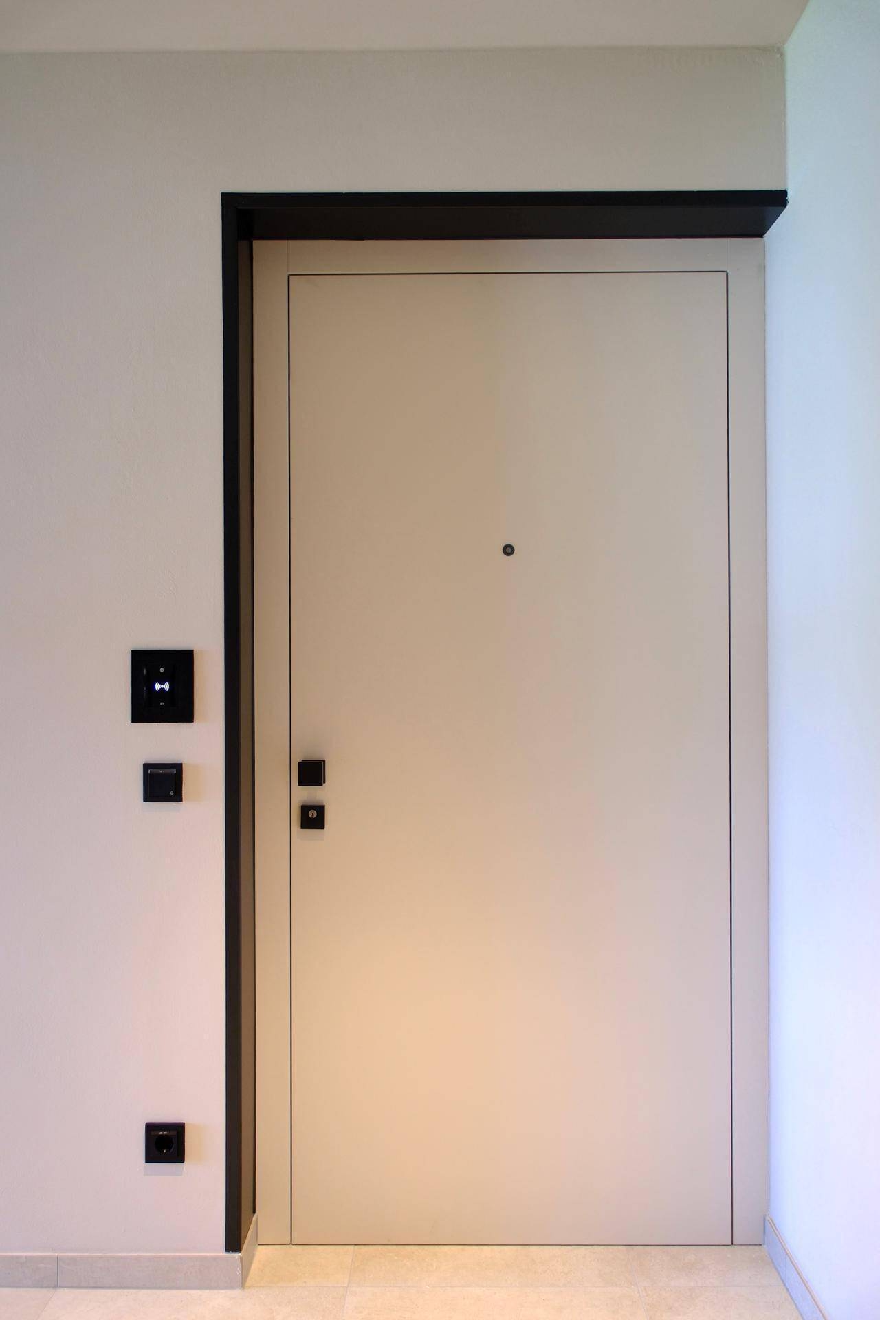 Moderne Eingangstür in hellem Beige mit schwarzem Rahmen und minimalistischen Schaltern.