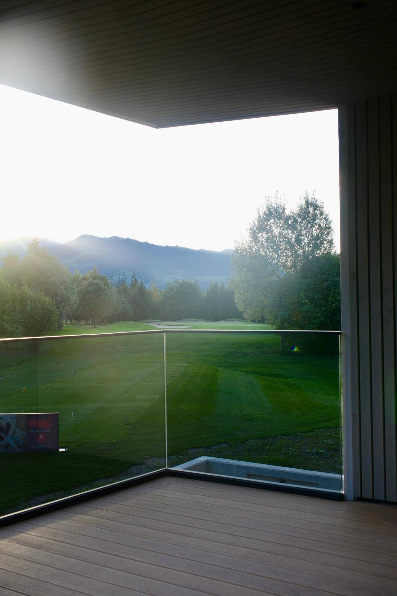 Sonniger Balkon mit Holzboden und Glasgeländer, bietet einen weiten Blick auf die umliegende Natur.