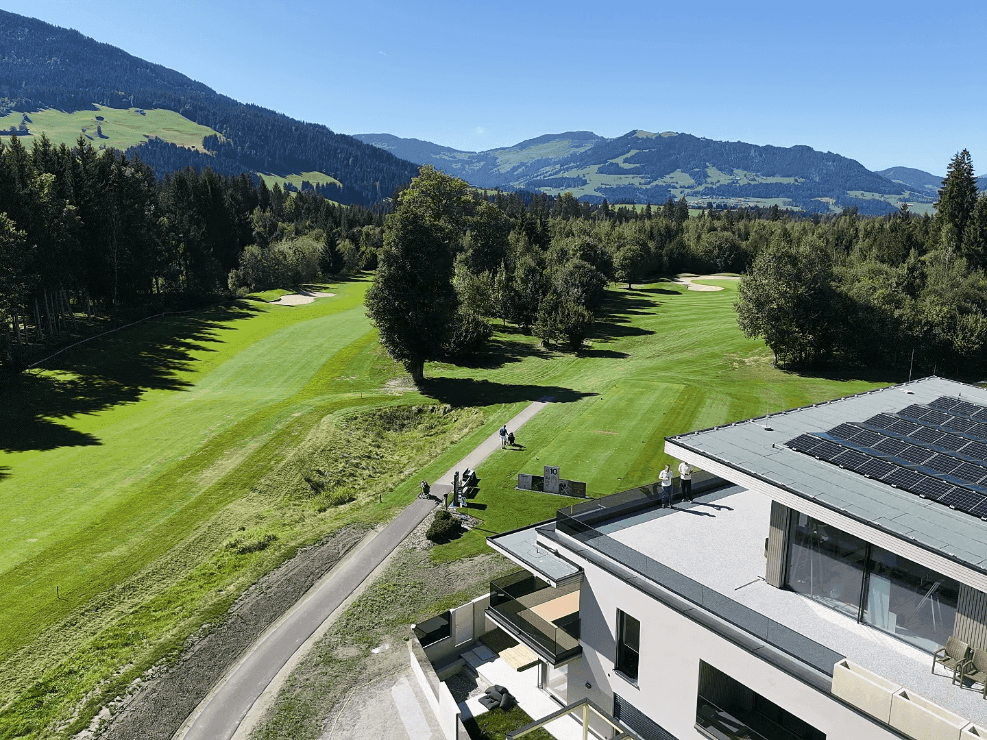 Moderne Wohnanlage mit Dachterrasse, Solaranlage und Panoramablick auf den Golfplatz und die Alpen.