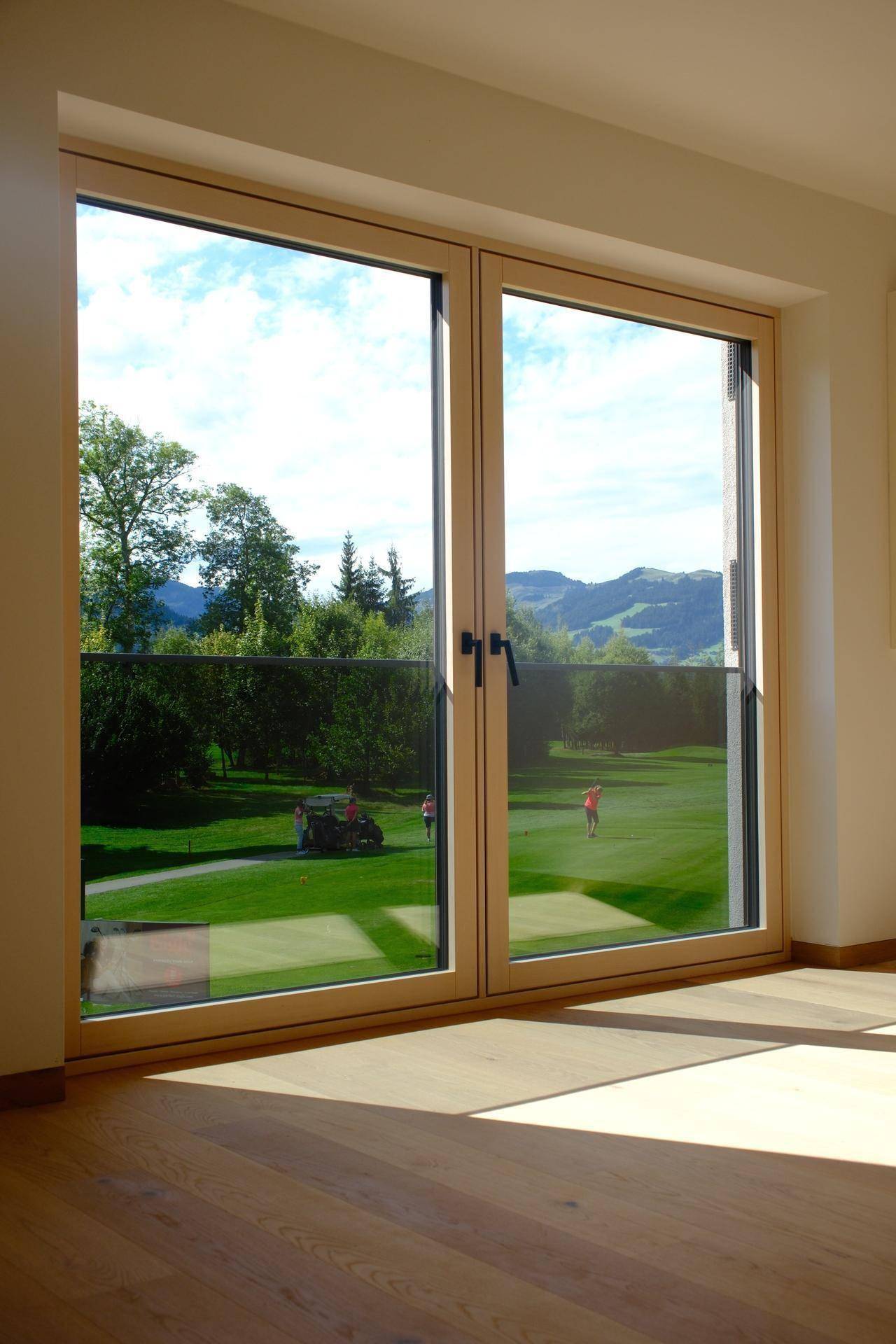 Helles Wohnzimmer mit Holzboden und großen Fenstern, die einen direkten Blick auf den Golfplatz bieten.
