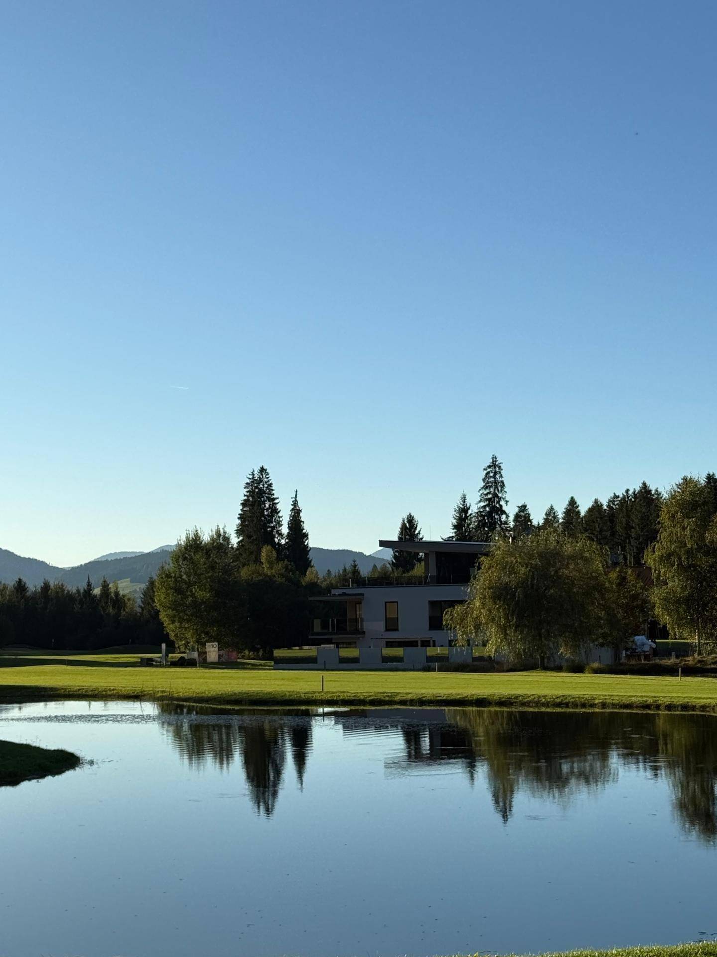 Modernes Gebäude am Teichrand mit Blick auf den Golfplatz und die umliegende Berglandschaft.