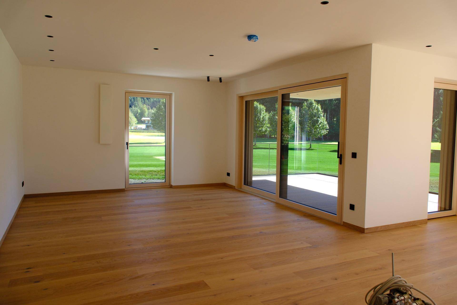 Großes, helles Wohnzimmer mit Holzboden und Zugang zu einer Terrasse mit Blick ins Grüne.