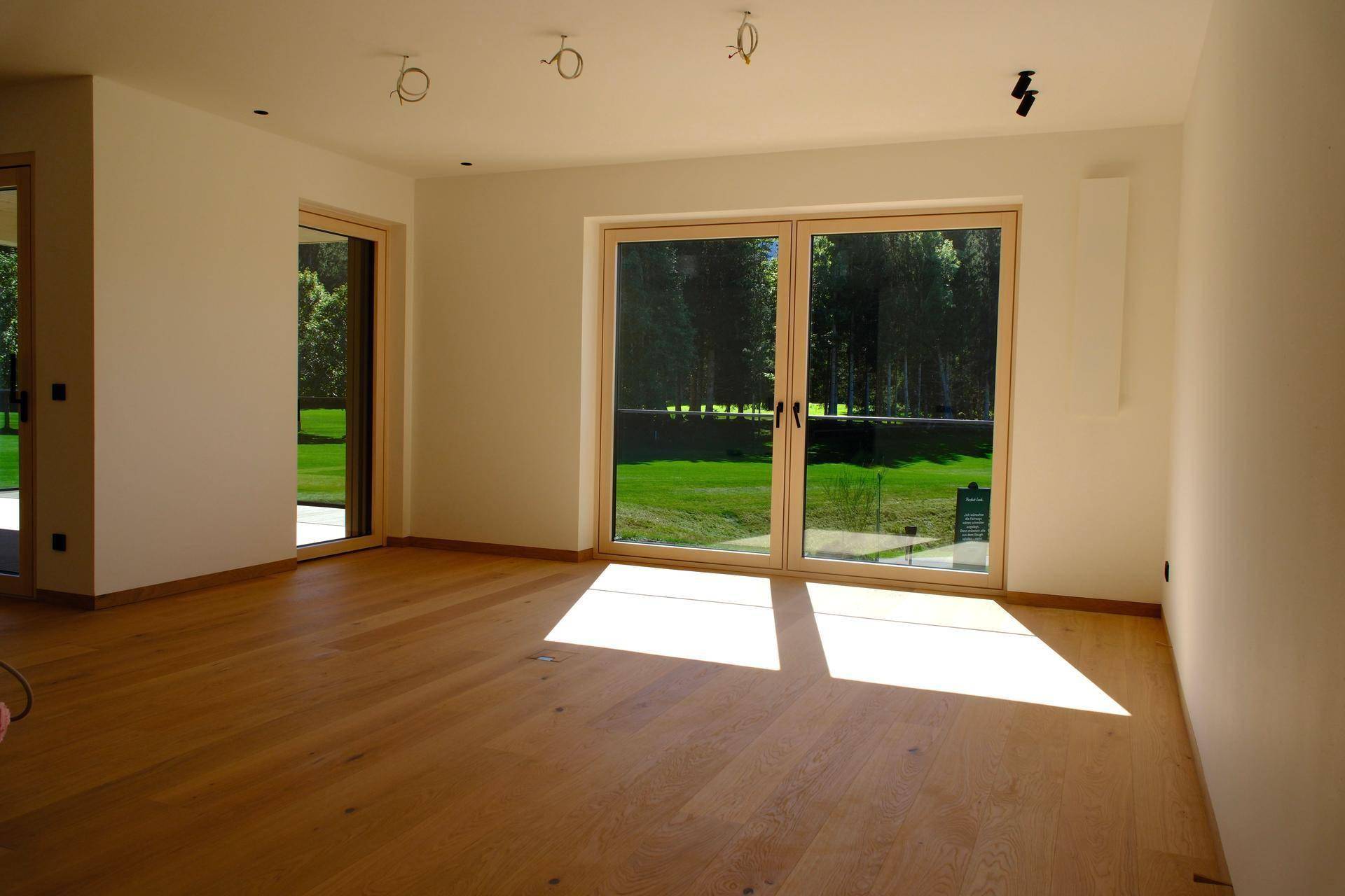 Lichtdurchflutetes Wohnzimmer mit Holzboden und großen Fenstern, die einen weiten Blick bieten.