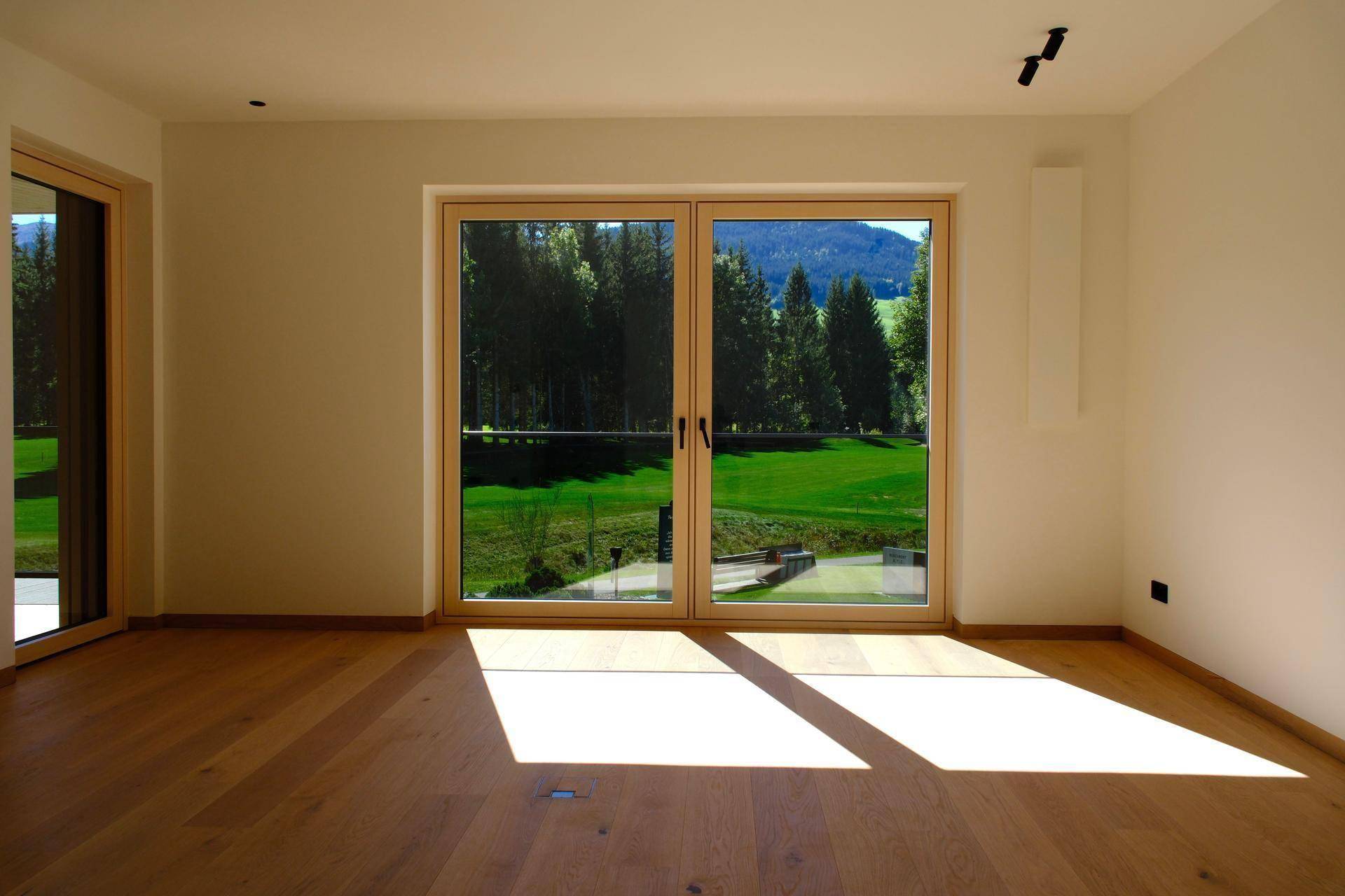 Helles Wohnzimmer mit Holzboden und Blick auf den grünen Golfplatz durch große Fenster.