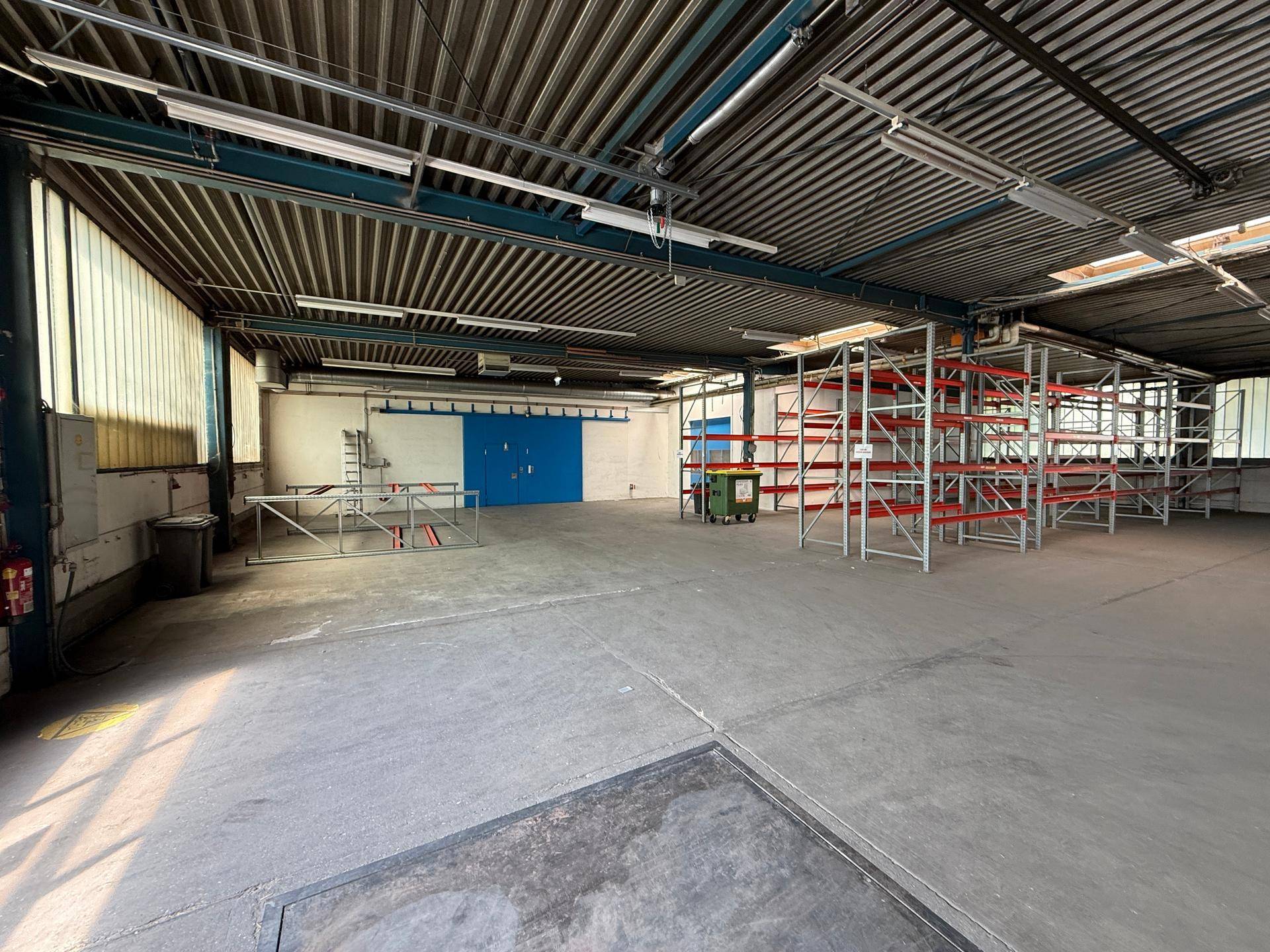 Geräumige Lagerhalle mit Betonboden, hohen Decken und leeren Regalen, bereit zur Nutzung.