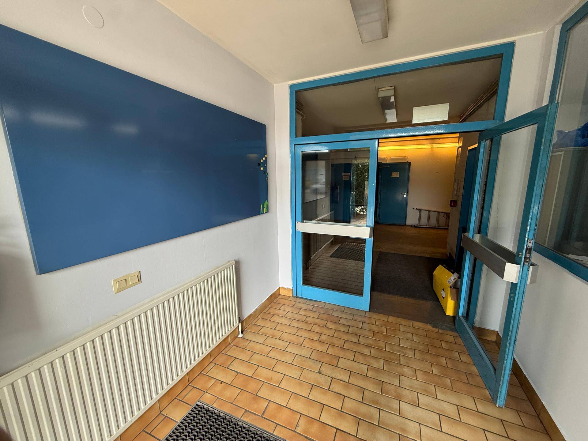 Eingangsbereich mit Fliesenboden, blauen Türen und einem Heizkörper, führt in weitere Räume.