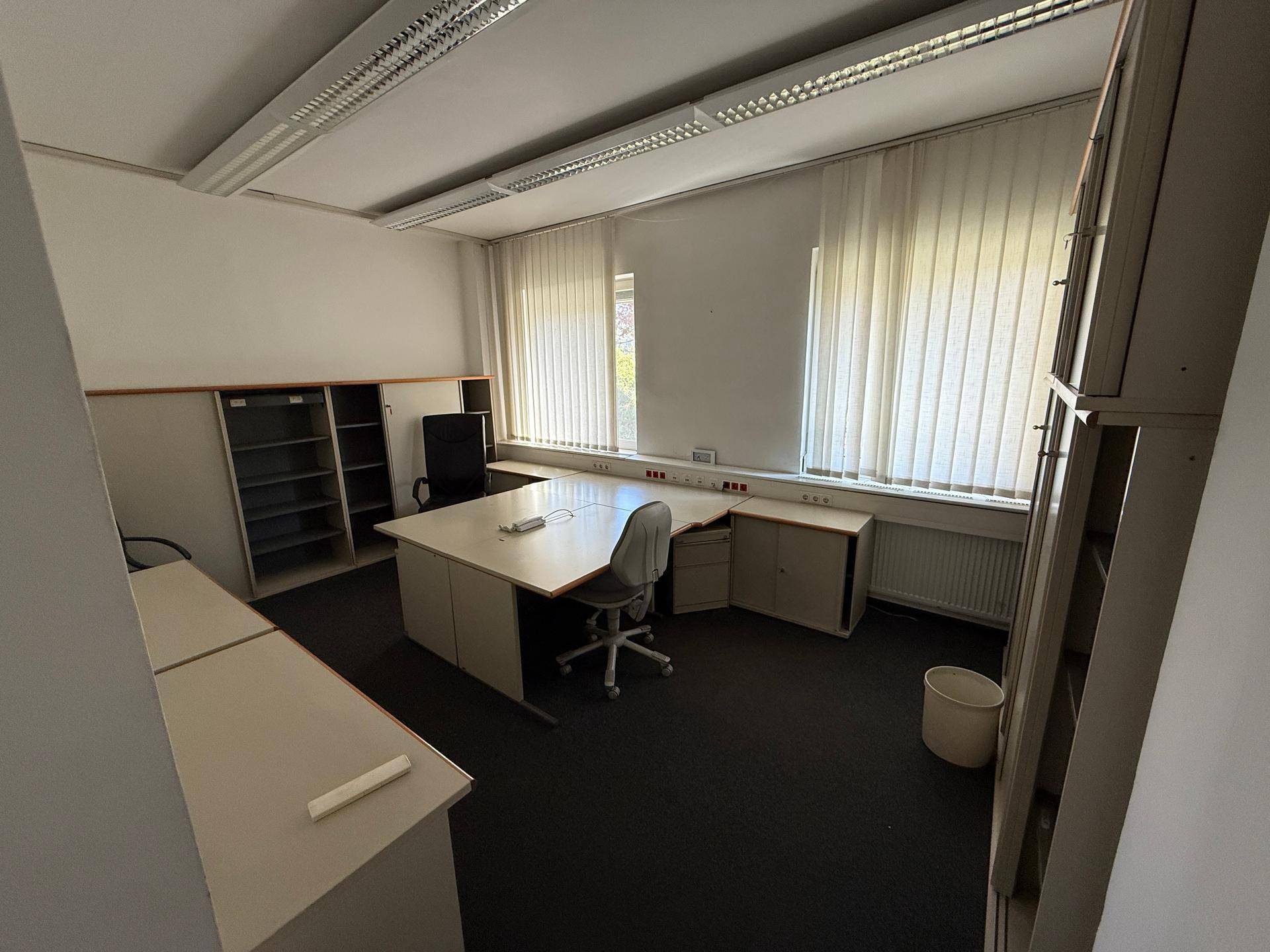 Helles Büro mit Teppichboden, Schreibtischen und großen Fenstern, bietet viel Arbeitsfläche.