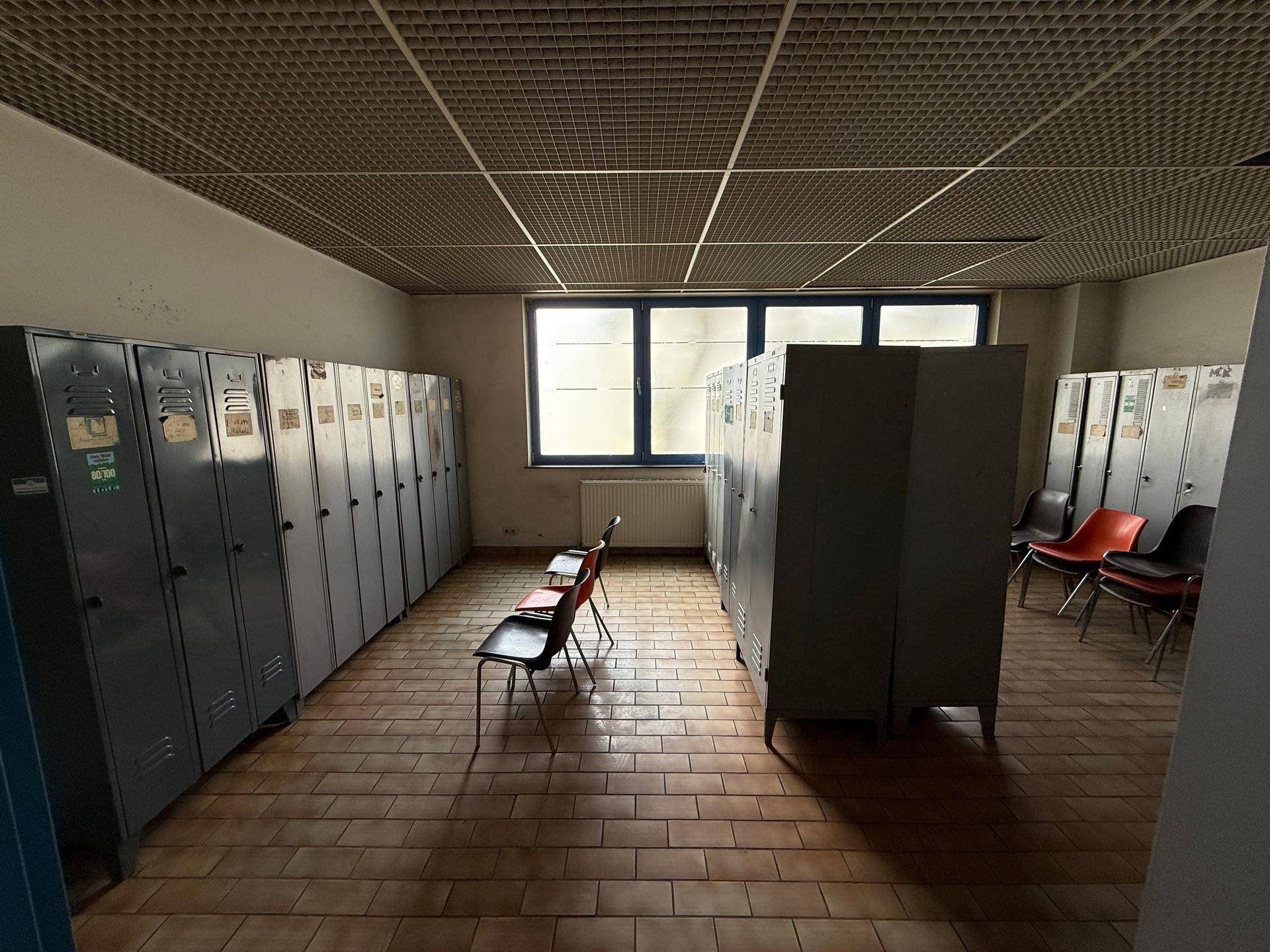 Umkleideraum mit Reihen von Spinden, Fliesenboden und einem Fenster für natürliches Licht.
