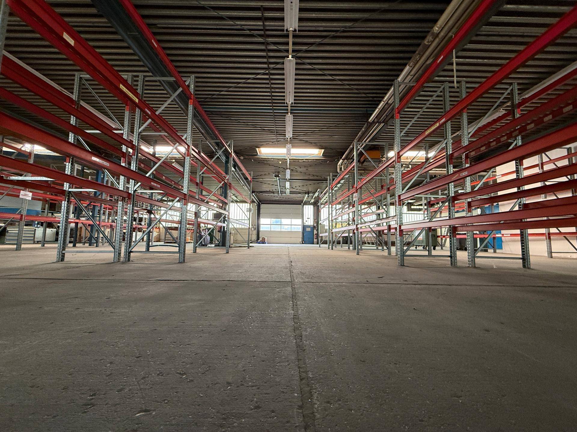 Lange Gänge in einer Lagerhalle mit Betonboden und hohen Regalsystemen, bereit für Waren.