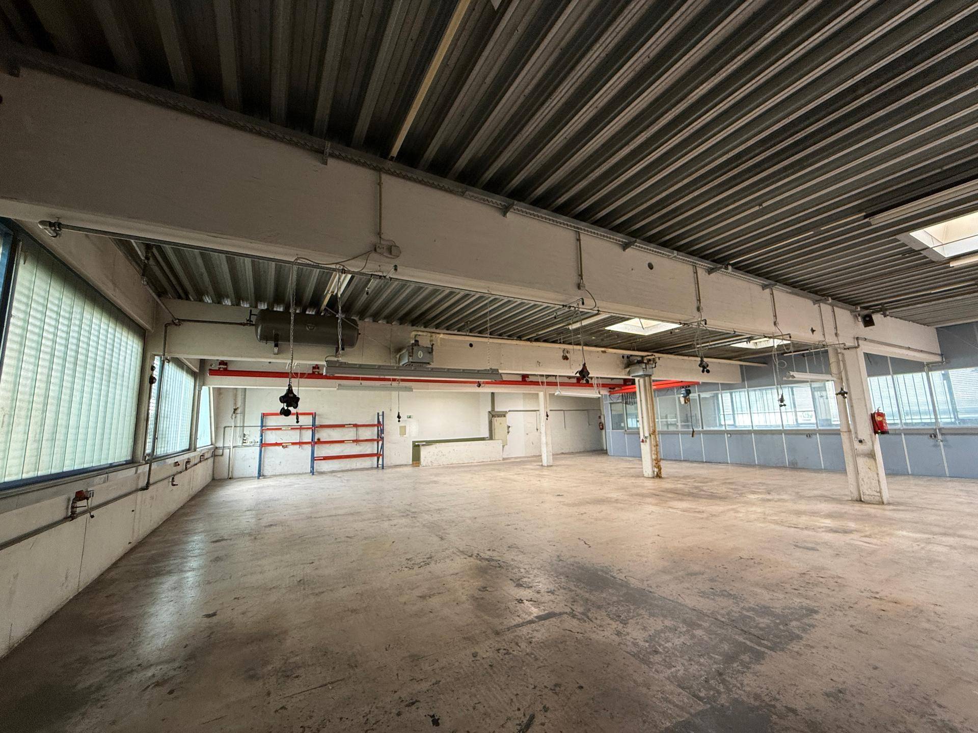 Weitläufige Lagerhalle mit Betonboden, hohen Decken und großen Fenstern, ideal für industrielle Nutzung.