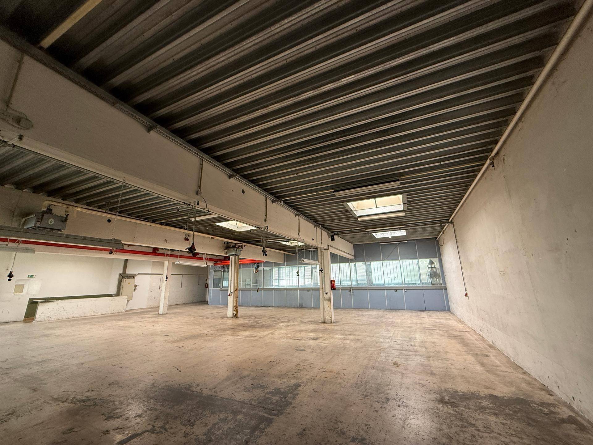 Geräumige Lagerhalle mit Betonboden, hohen Decken und Oberlichtern, bietet viel Platz für Lagerung.