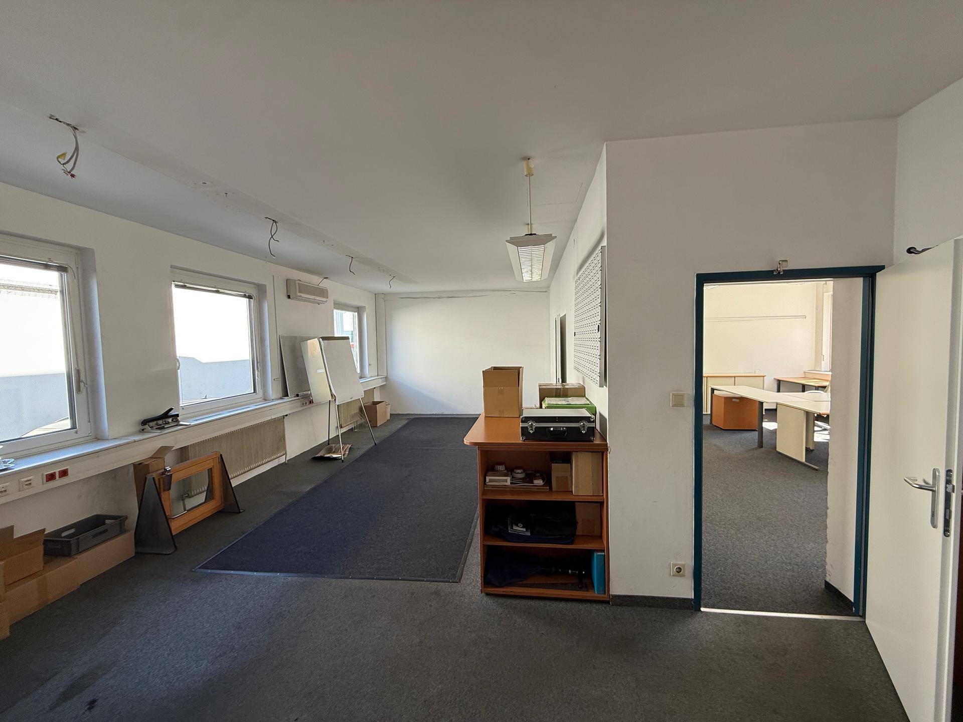 Geräumiges Büro mit Teppichboden, weißen Wänden und mehreren Fenstern für Tageslicht.