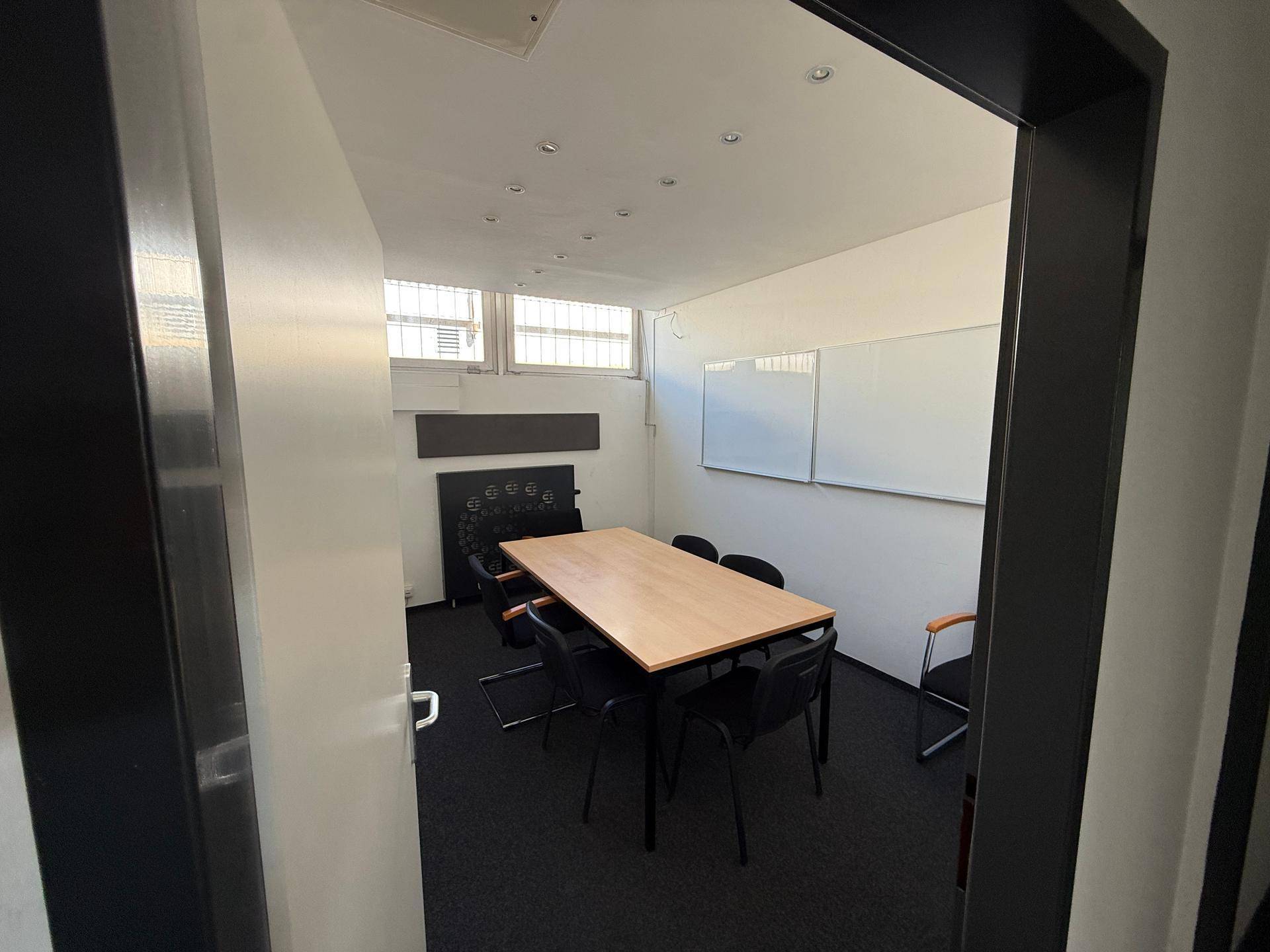 Konferenzraum mit Teppichboden, großem Holztisch und Whiteboards an der Wand.