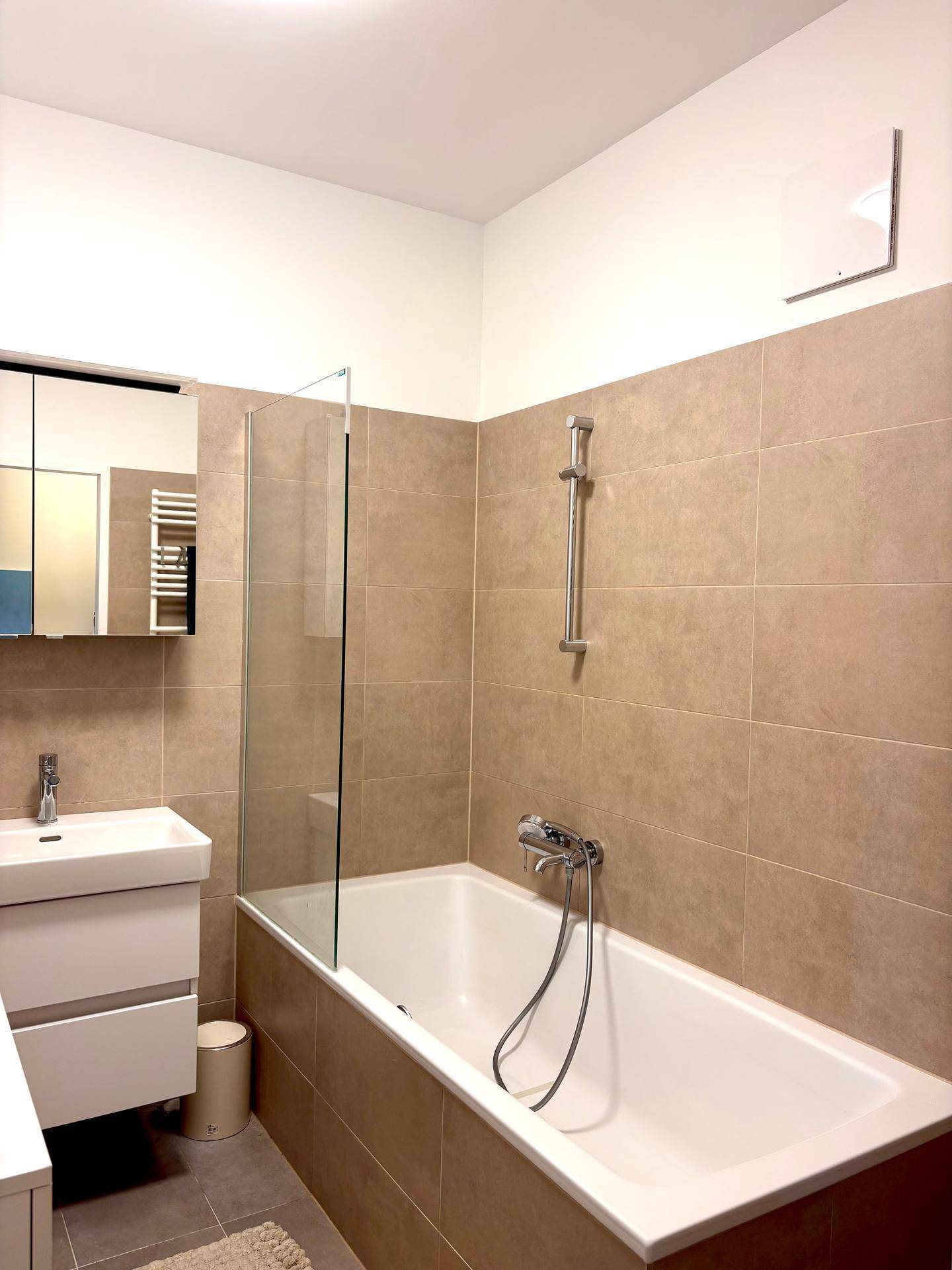 Modernes Badezimmer mit Badewanne, Duschabtrennung und beigefarbenen Fliesen.