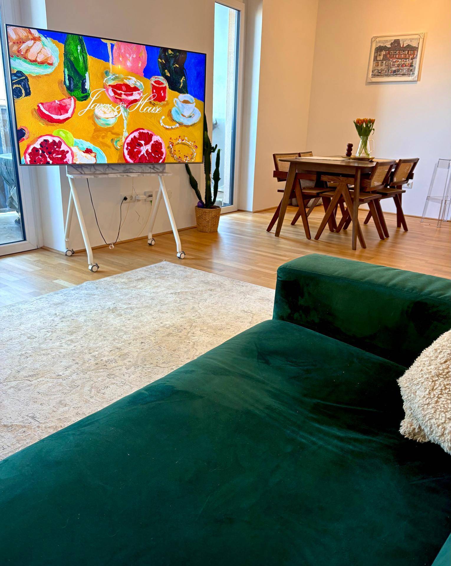 Heller Wohn-Essbereich mit grünem Sofa, Holzboden und modernem Fernseher.