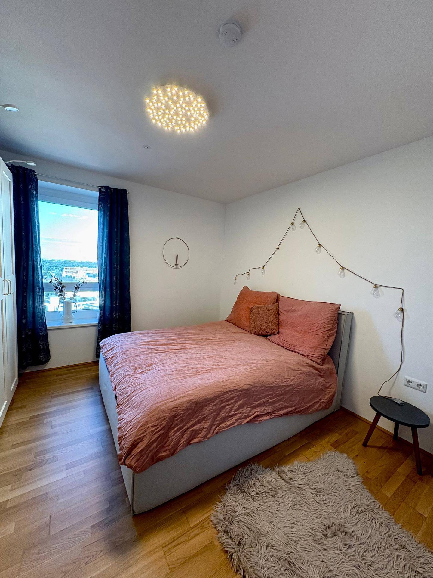 Gemütliches Schlafzimmer mit Holzboden, großem Fenster und indirekter Beleuchtung.
