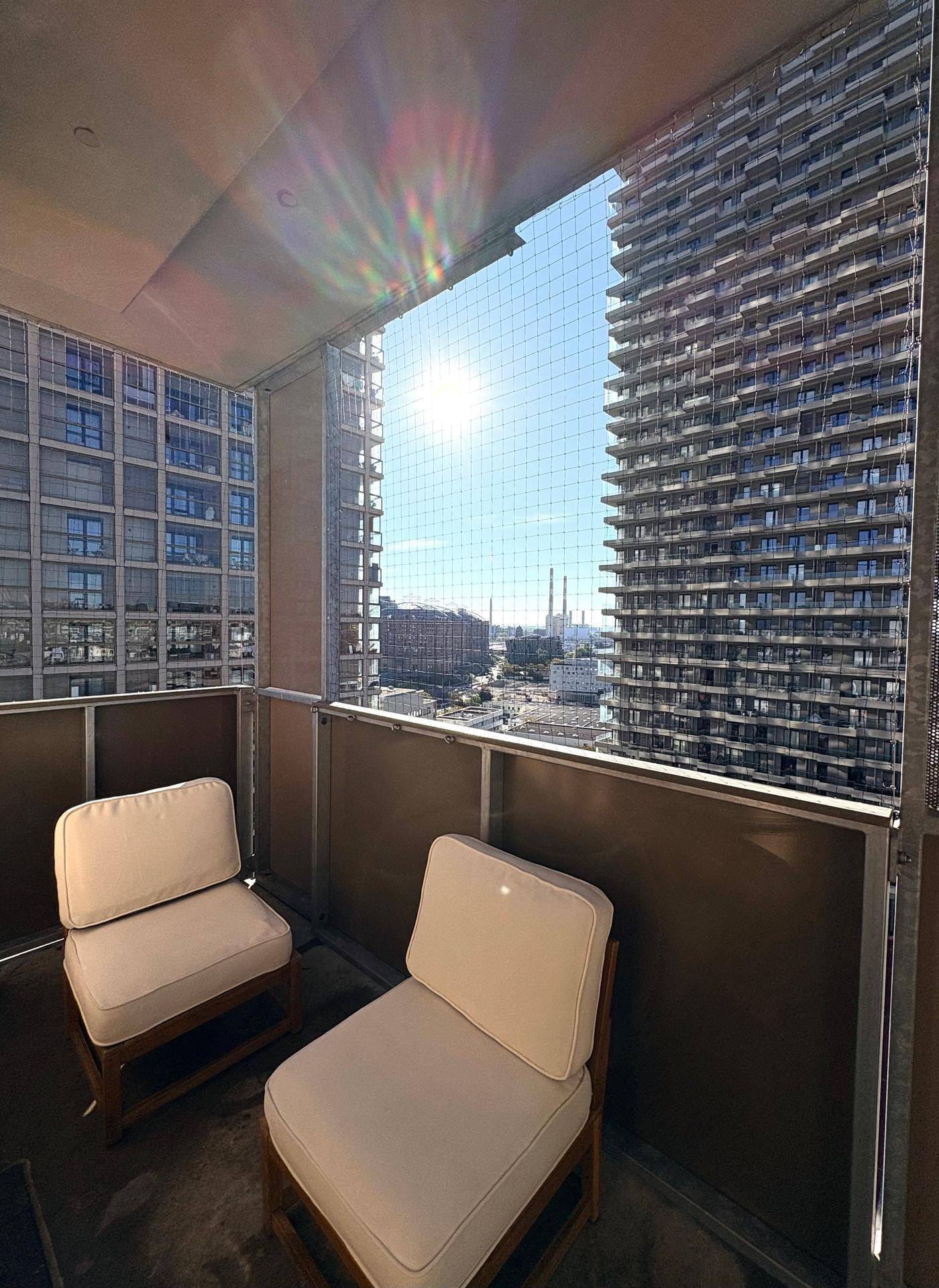 Sonniger Balkon mit bequemen Sesseln und Blick auf moderne Hochhäuser.