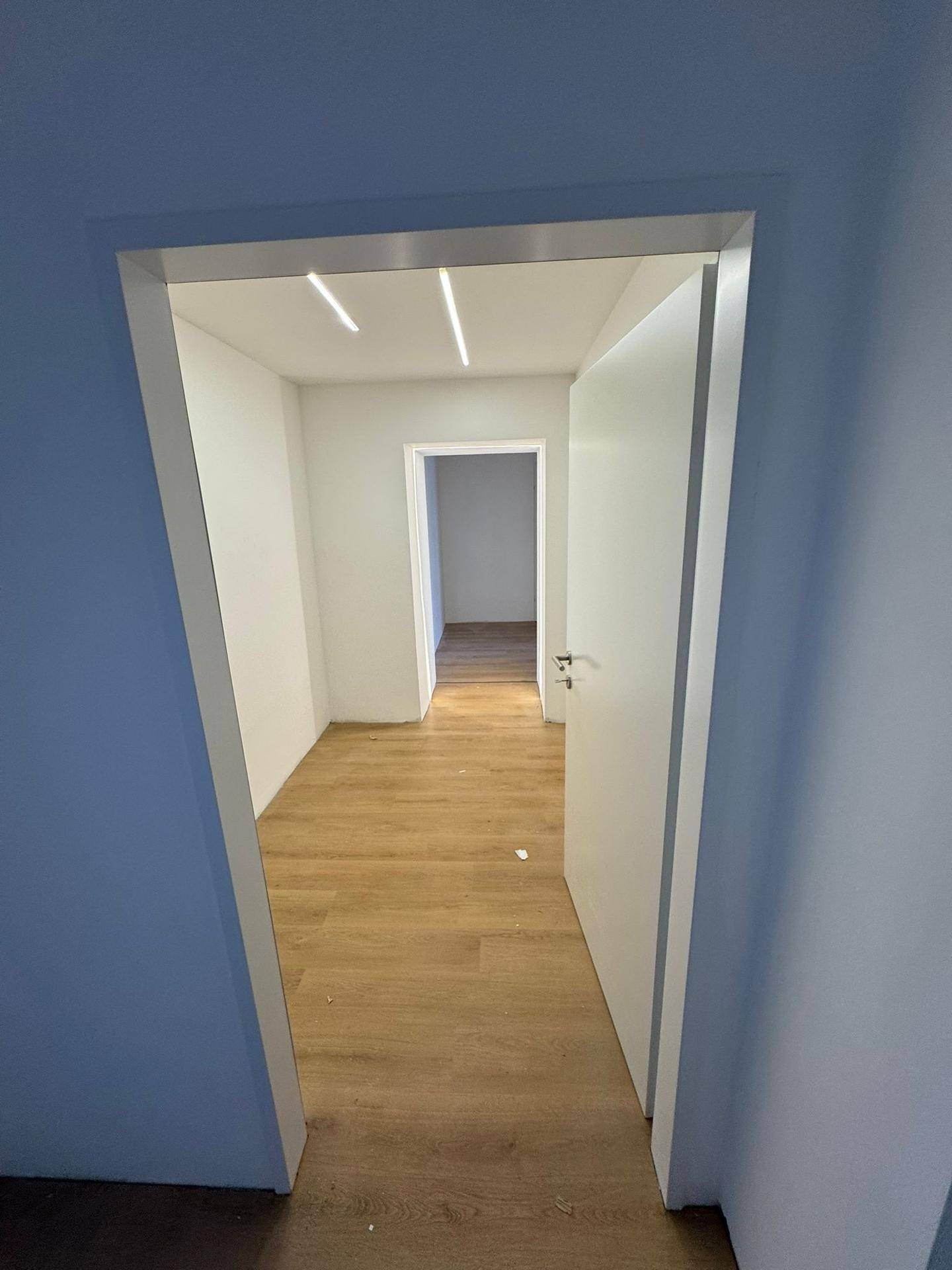 Heller Flur mit Laminatboden und weißen Wänden, der zu weiteren Räumen in der Wohnung führt.