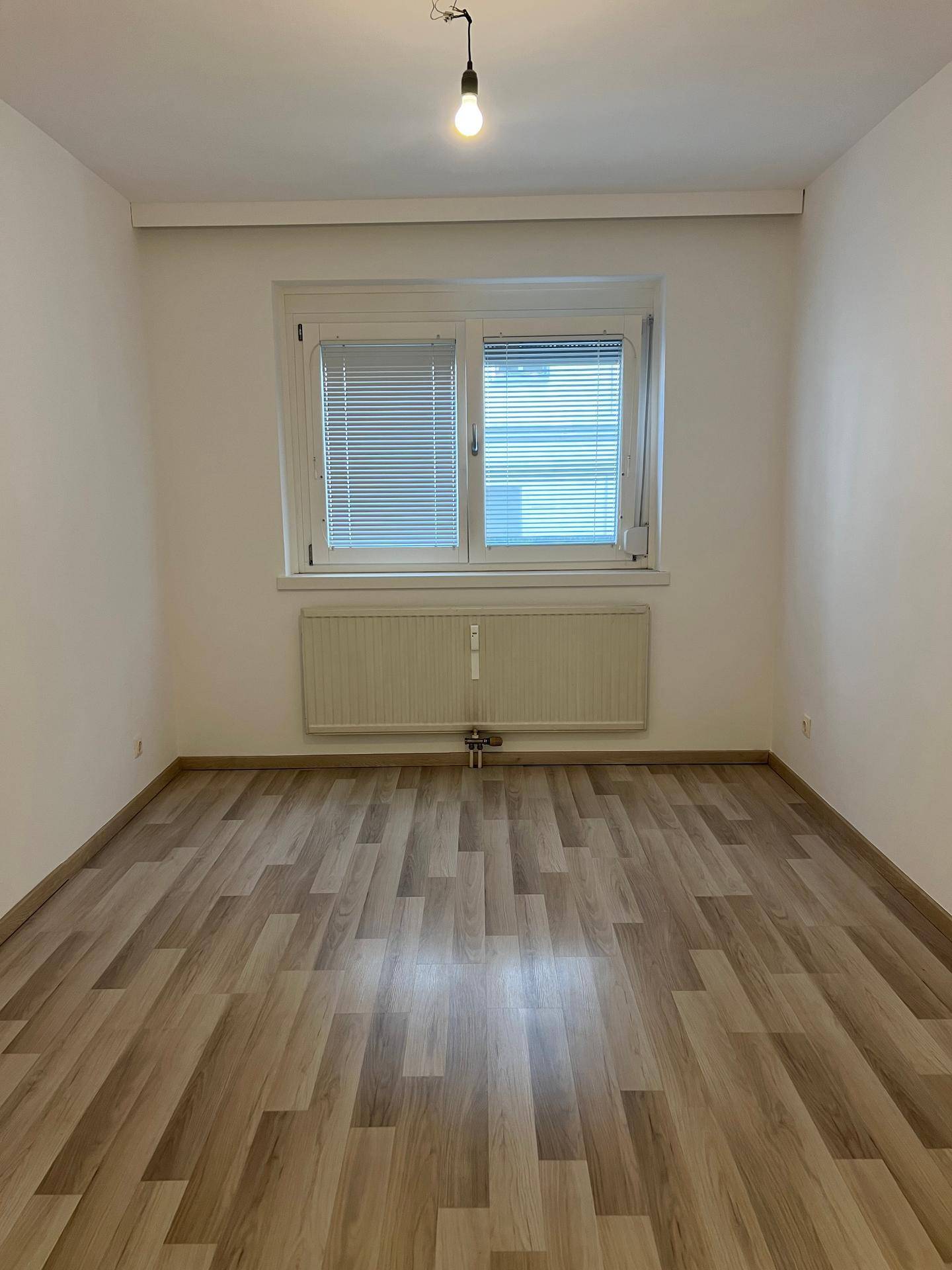 Helles Zimmer mit Laminatboden, großem Fenster und Heizkörper, bereit zur individuellen Gestaltung.
